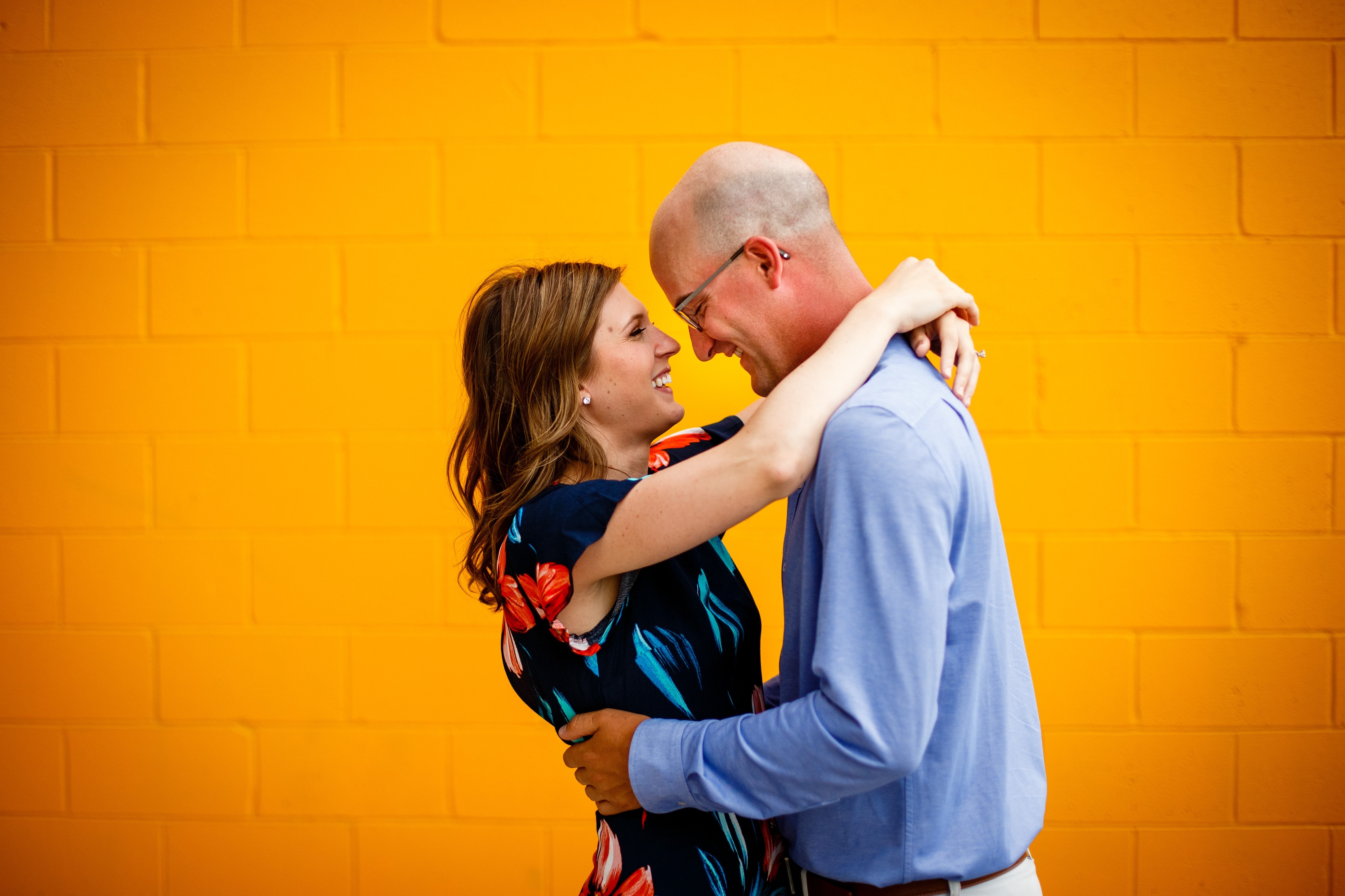 Erica and Cody embrace in front of a tangerine colored wall during their summertime engagement photos in Royal Oak, Michigan