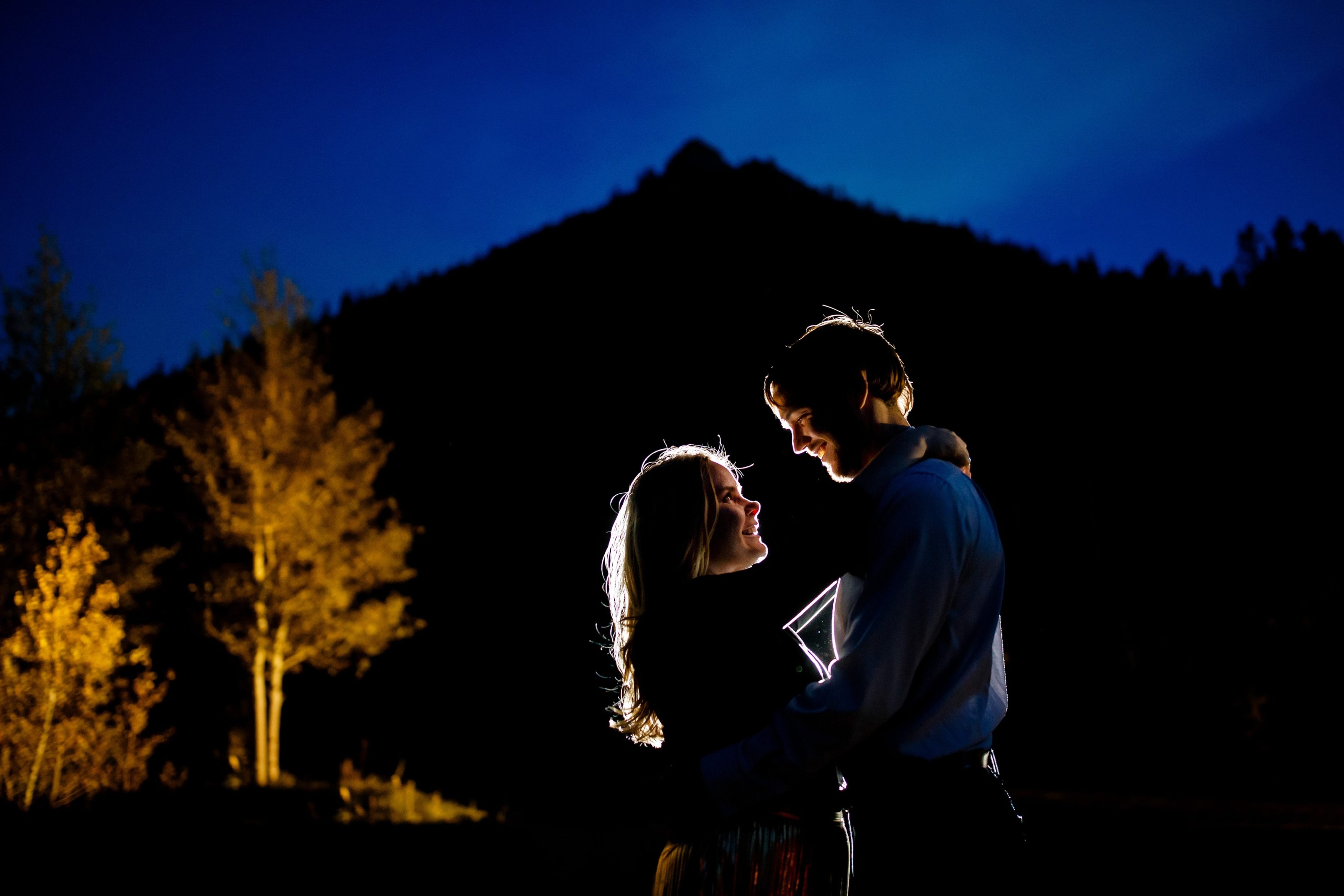 Coza and Joel are illuminated near a grove of aspen trees at twilight during their fall Golden engaement at Golden Gate Canyon State Park