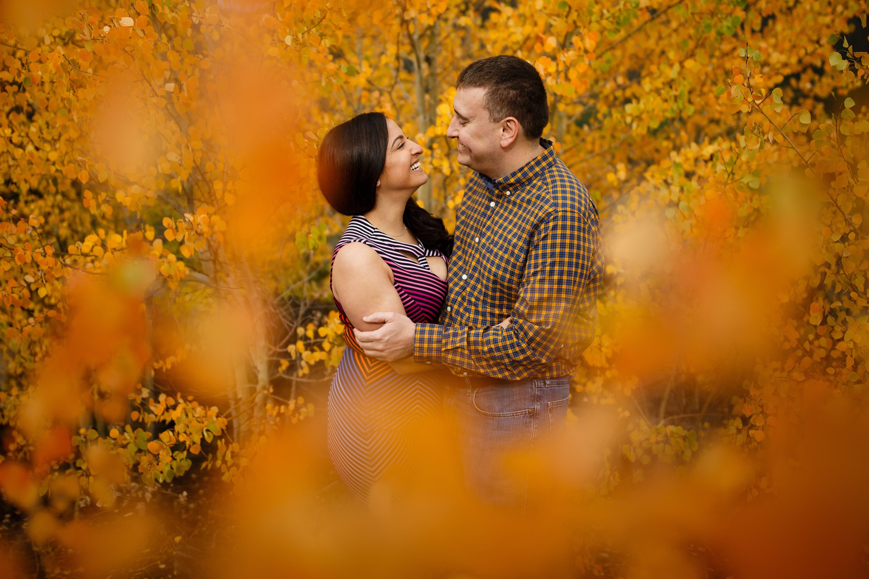 Joseph and Shabnam share a laugh in a grove of yellow aspen trees during their Breckenridge fall colors engagement photos on Gold Hill