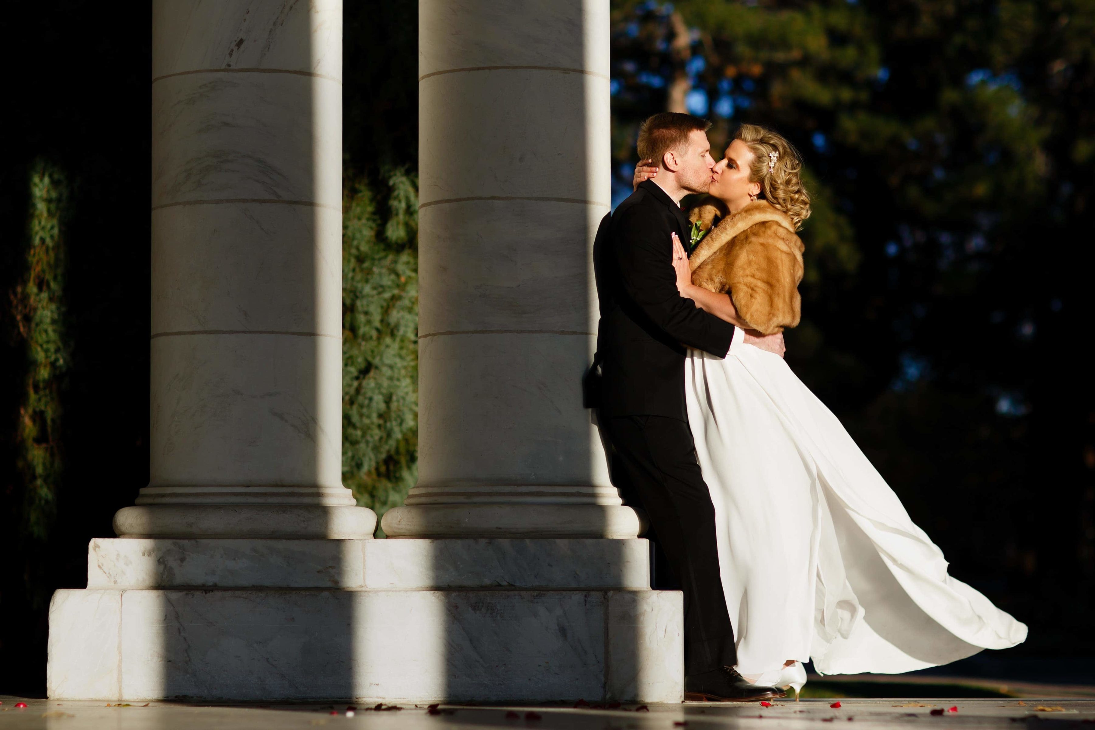 Sarah uses a fur shall to stay warm and embraces Ryan for a kiss in the sunlight after their fall Cheesman Park Wedding