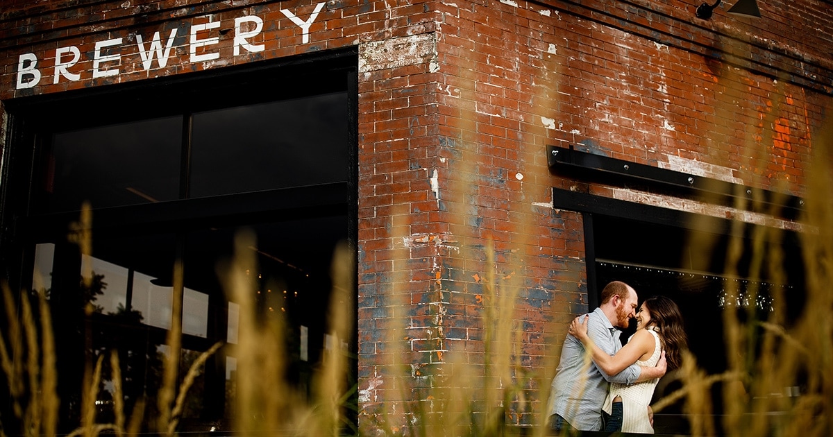 Chris and Angie embrace outside of Briar Common Brewery in the Jefferson Park neighborhood of Denver during their engagement photos