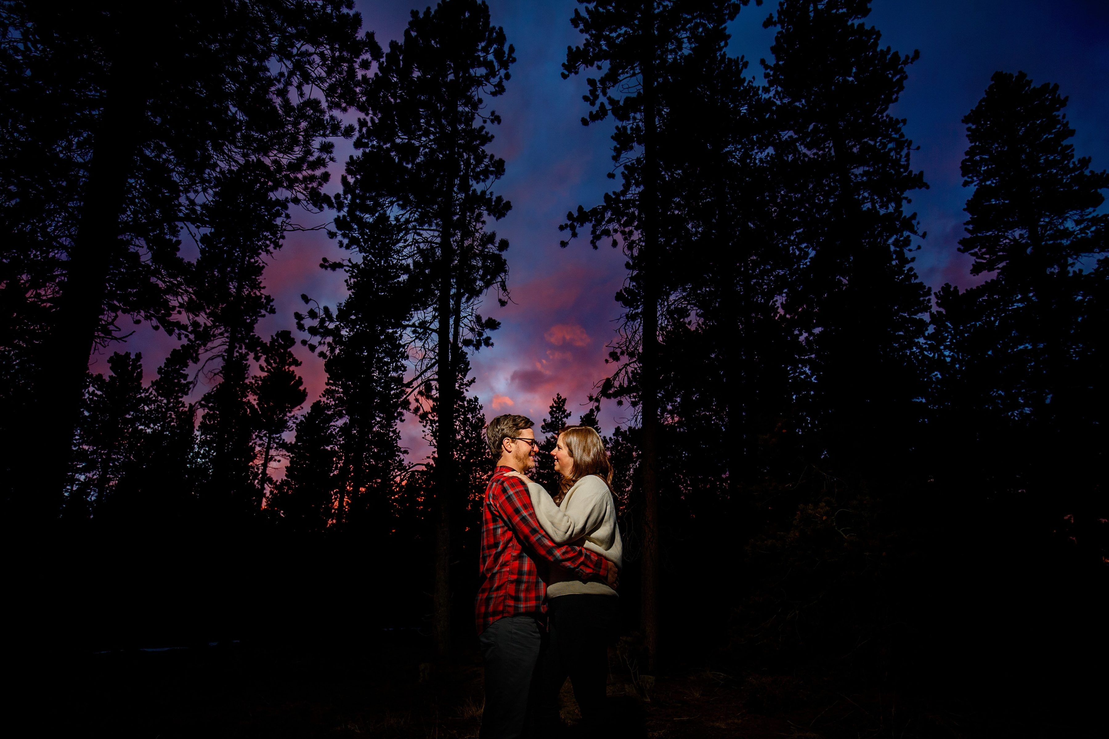 Kate and Brian pose together in a grove of trees as the sun sets at Golden Gate Canyon State Park