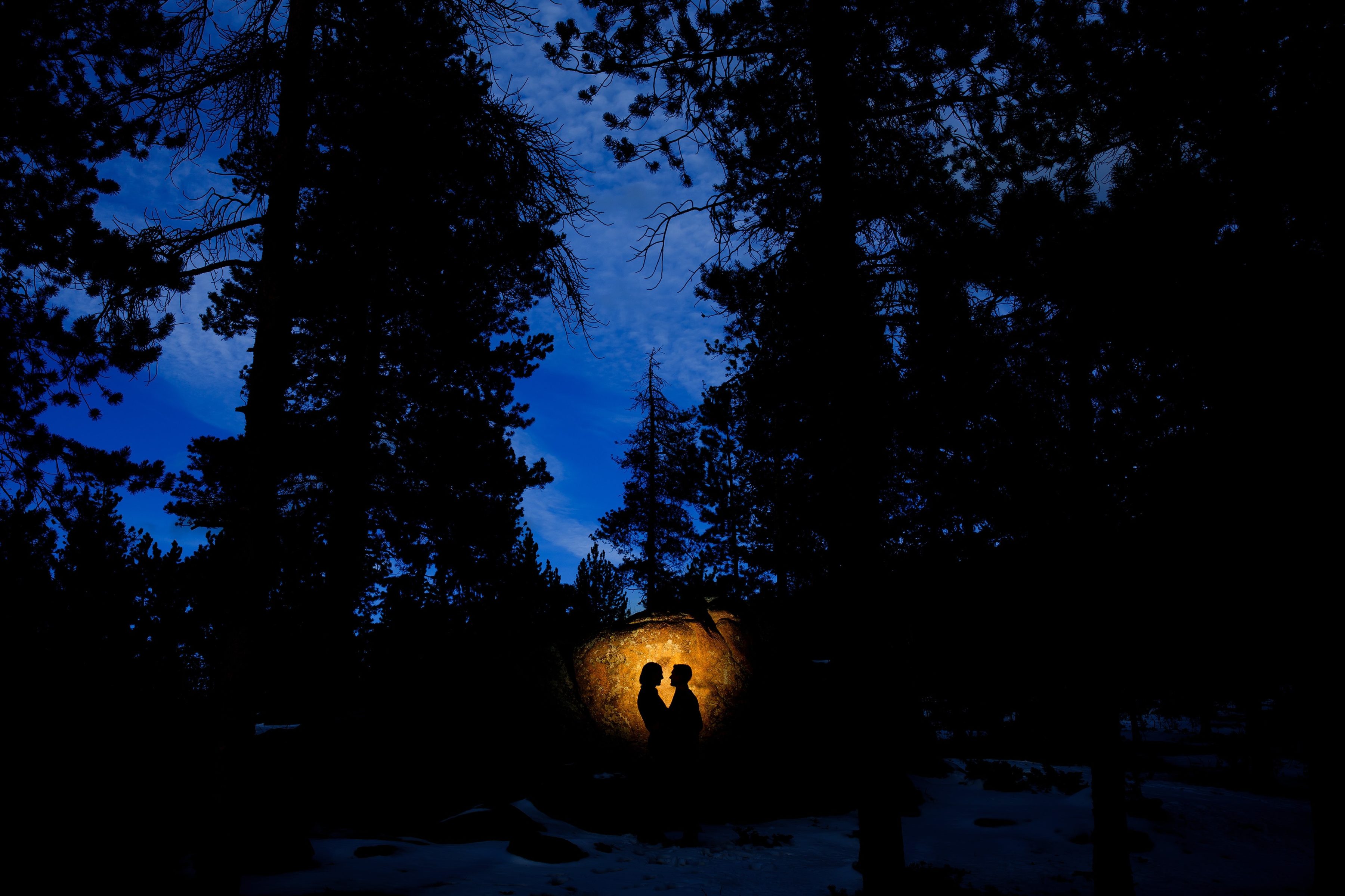 A couple are silhouetted against a rock in Evergreen during their creative engagement photo session
