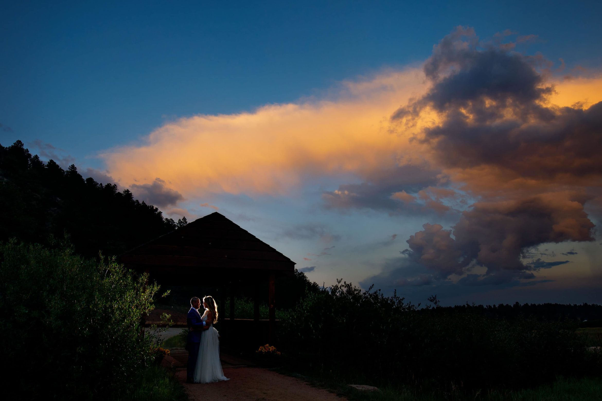 The couple are illuminated on the bridge at sunset during their summer barn wedding at Deer Creek Valley Ranch