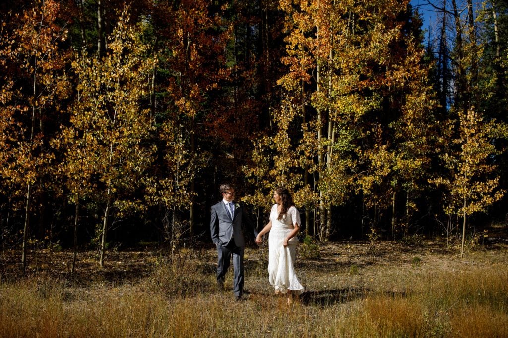 The newlyweds walk together near a grove of colorful aspen trees during their fall Blackstone Rivers Ranch wedding in Idaho Springs Colorado