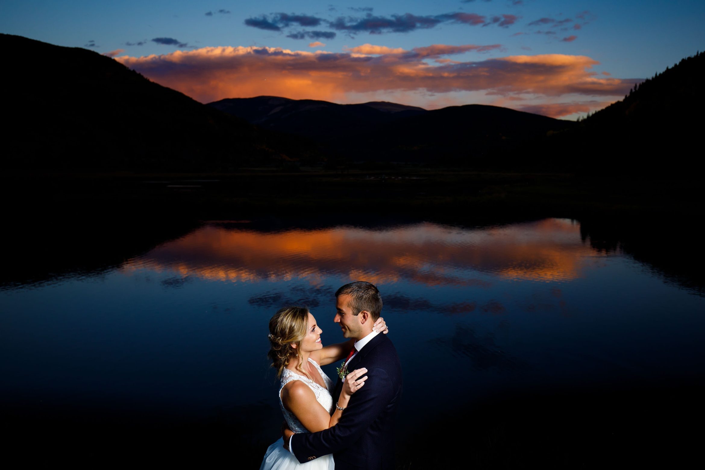 A sunset is reflected on the pond at Camp Hale as the couple poses during their fall wedding