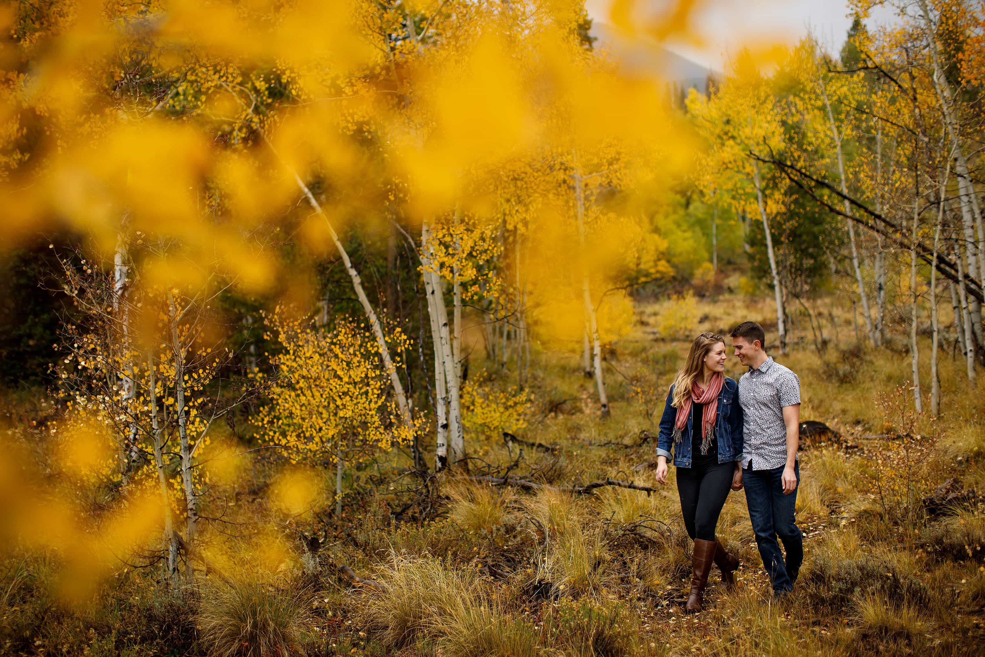 Holly and Hayden walk in a grove of aspen trees near Meadow Creek Trailhead in Frisco during their engagement photos