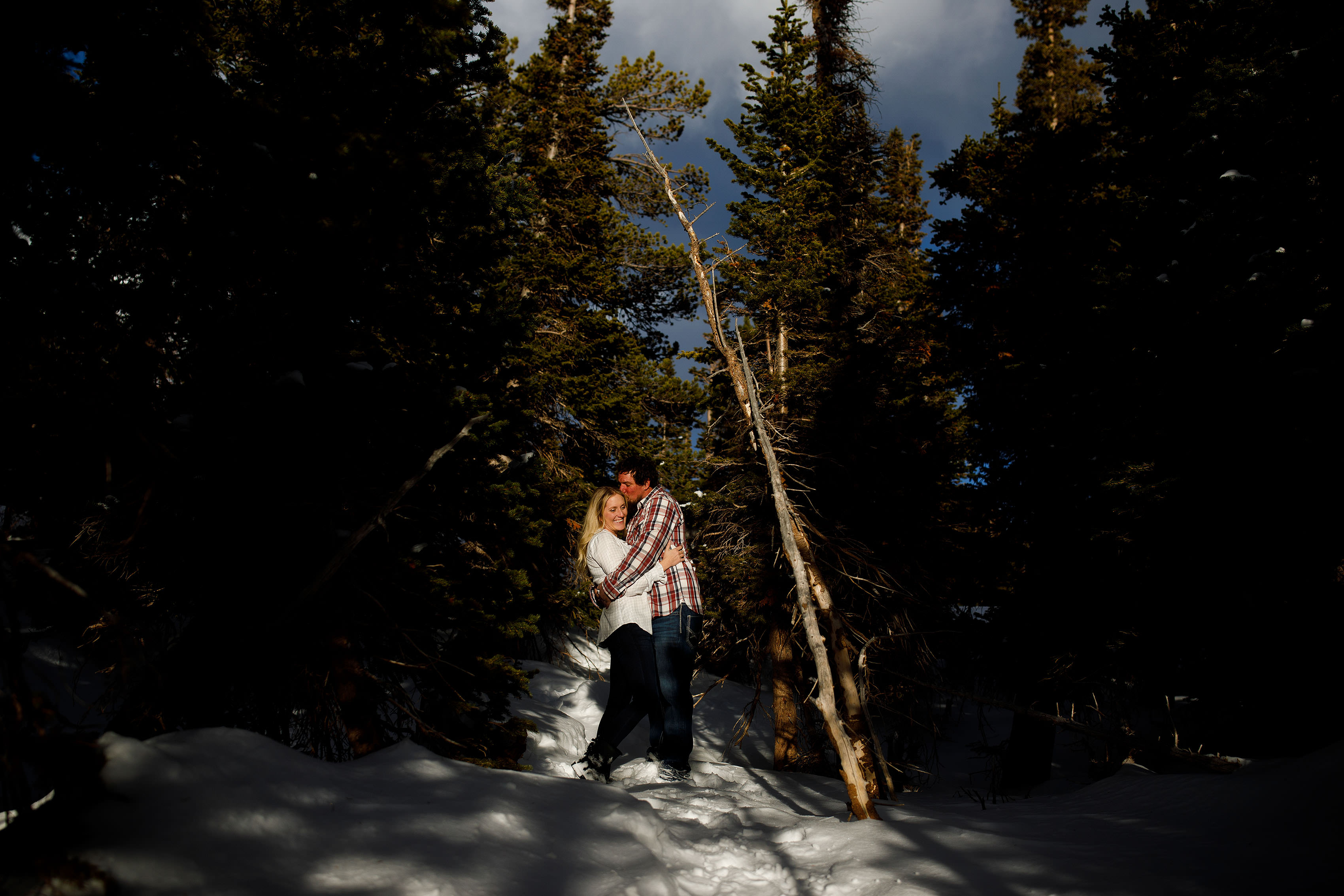 Aaron kisses Meaghan in the trees at Brainard Lake during their winter engagement session in Colorado