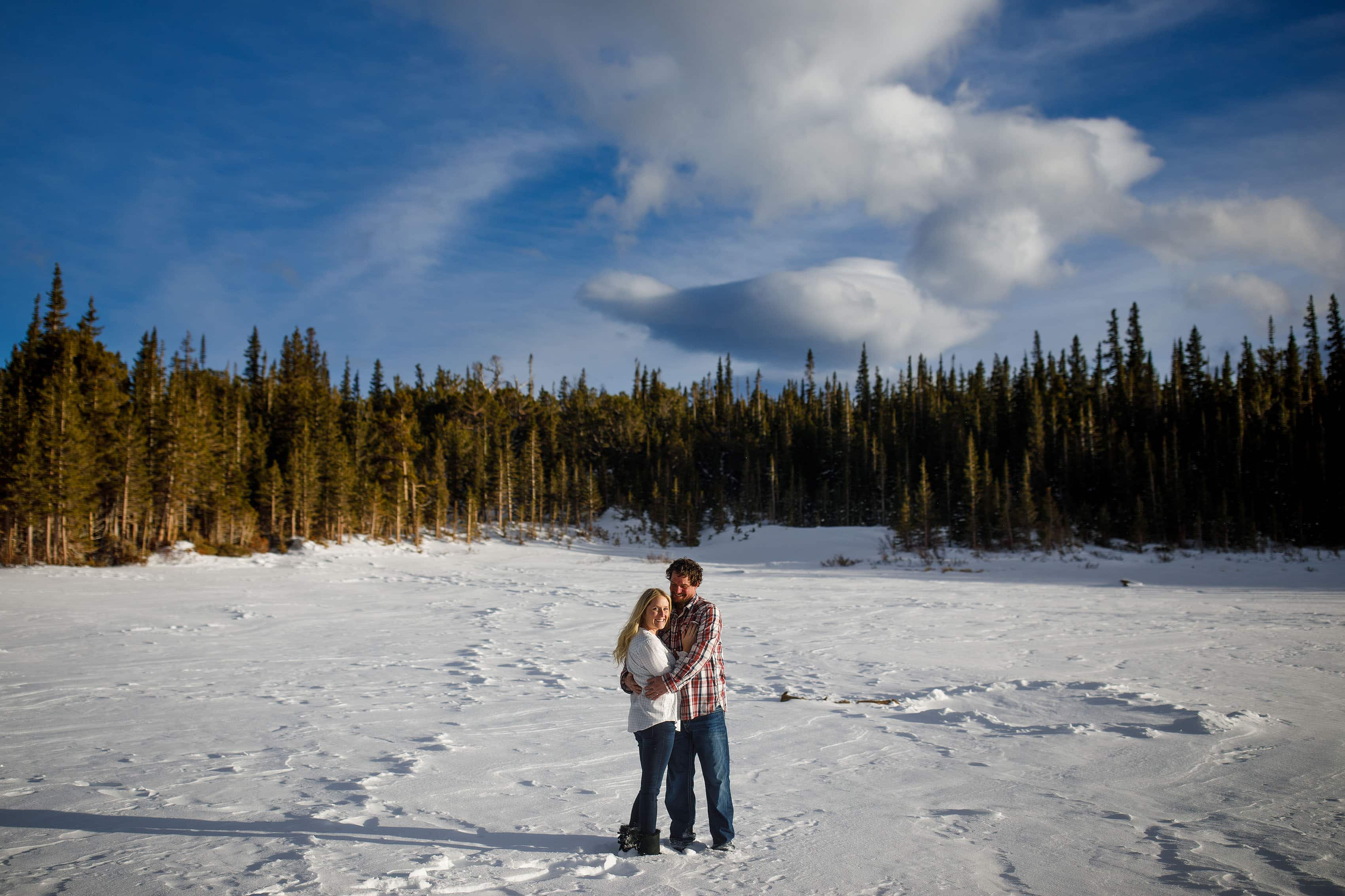 Meaghan smiles while Aaron keeps her wam while they stand on snow covered Brainard Lake during their engagement session near Ward, Colorado