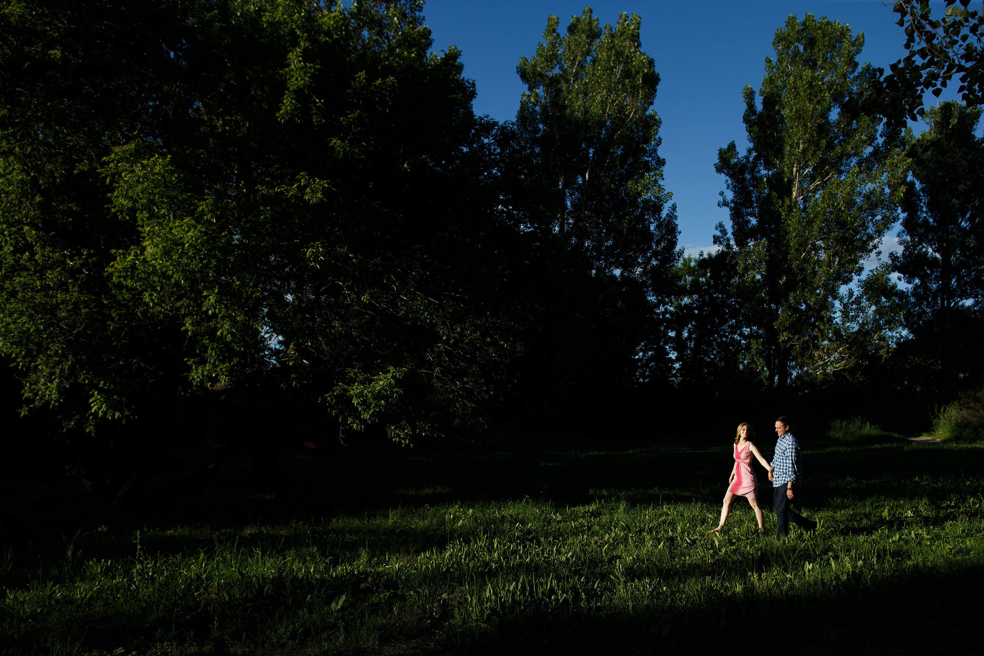 Kristy and Jonathan walk together towards sunlight in a grove of trees at Eldorado Springs