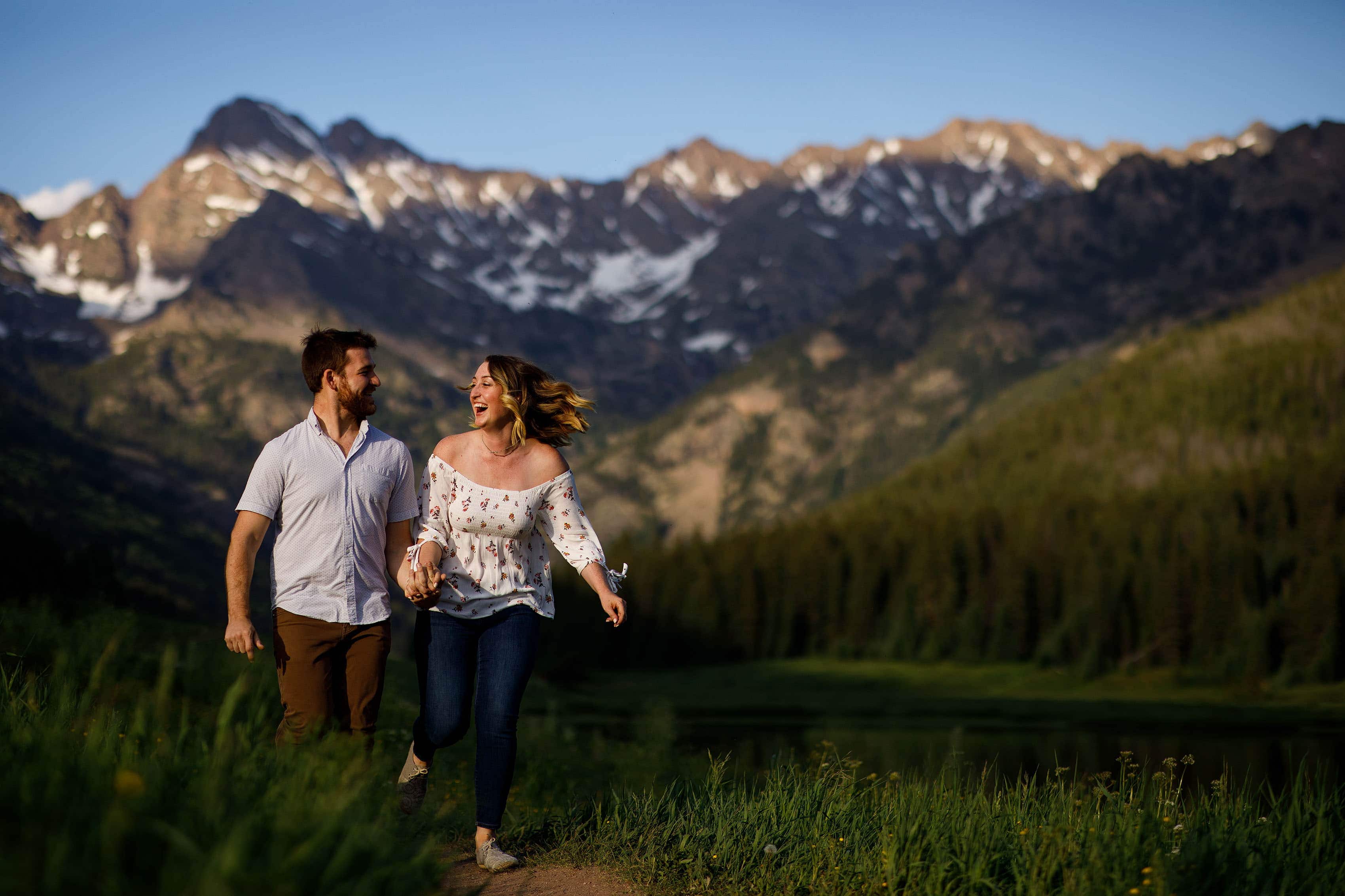 Laura and Ryan laugh and run at Piney River Ranch during their engagement session near Vail, Colorado