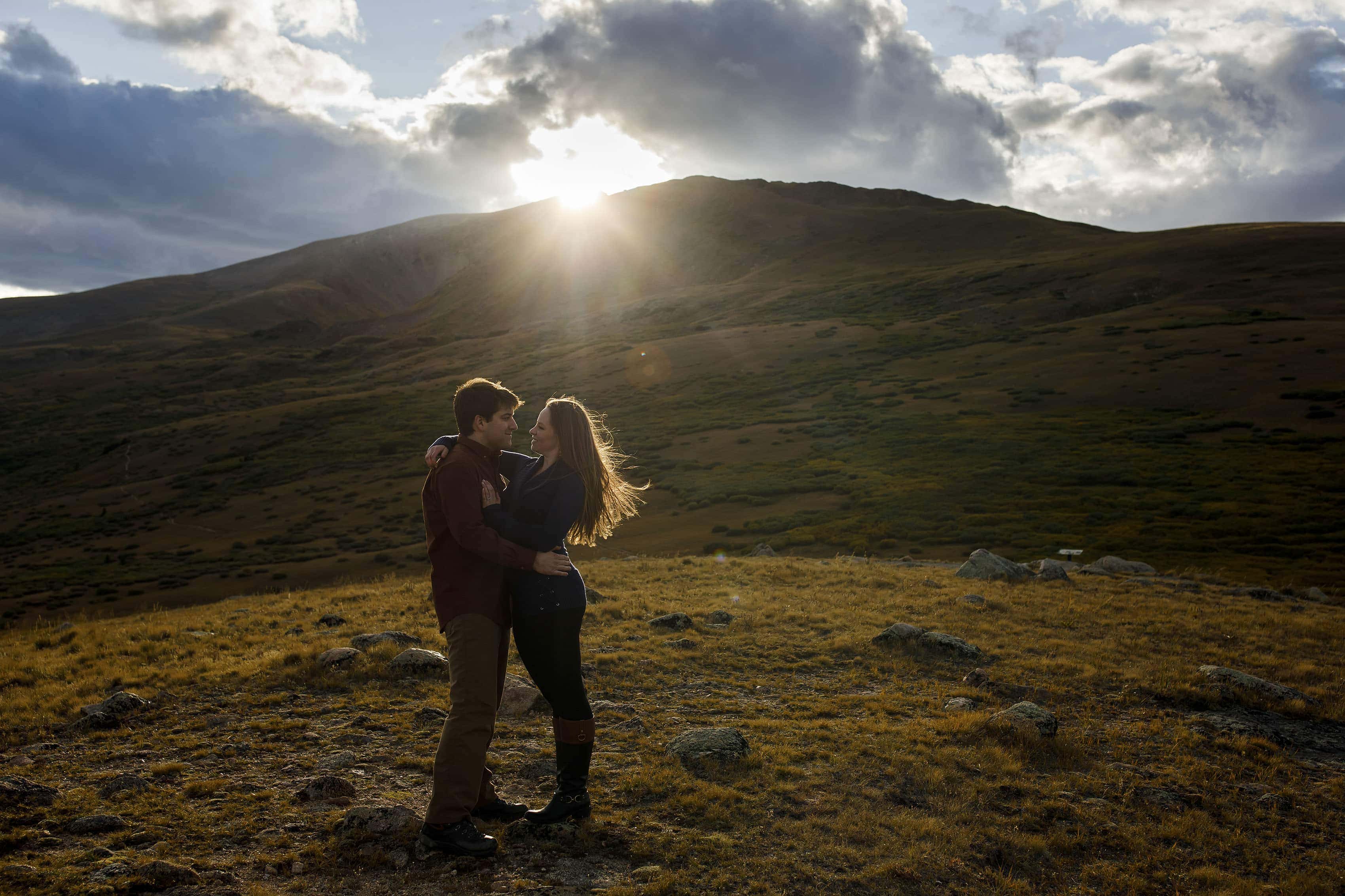 The sun sets over Square Top Mountain as a couple poses during their engagement photos at Guanella Pass