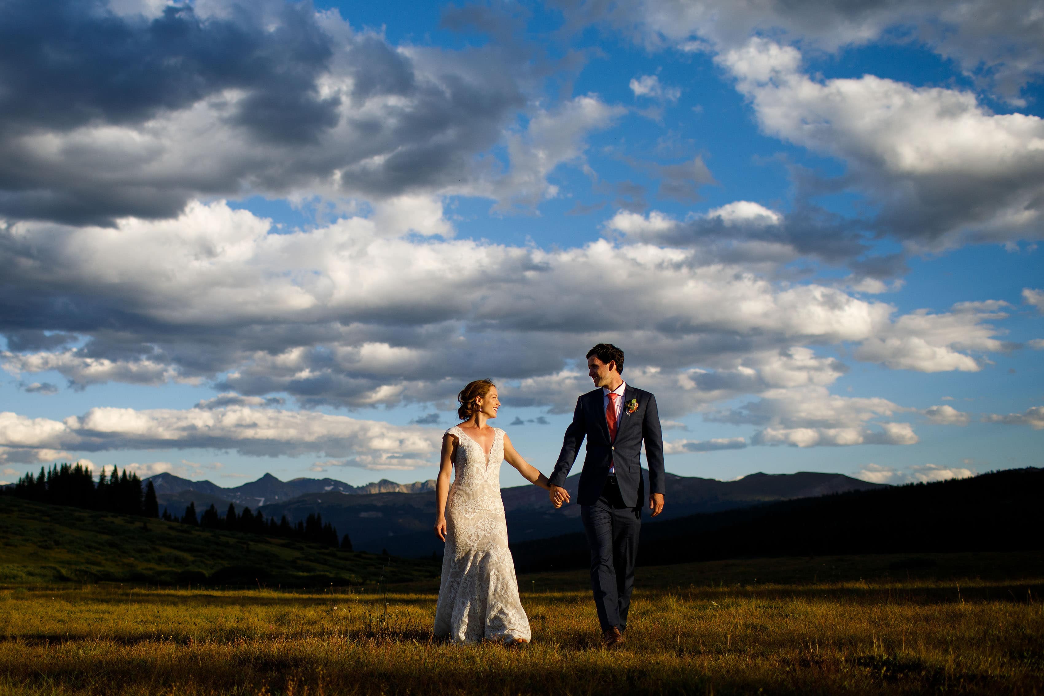 A bride and groom walk hand-in-hand as the sun sets atop Shrine Pass near Vail, Colorado