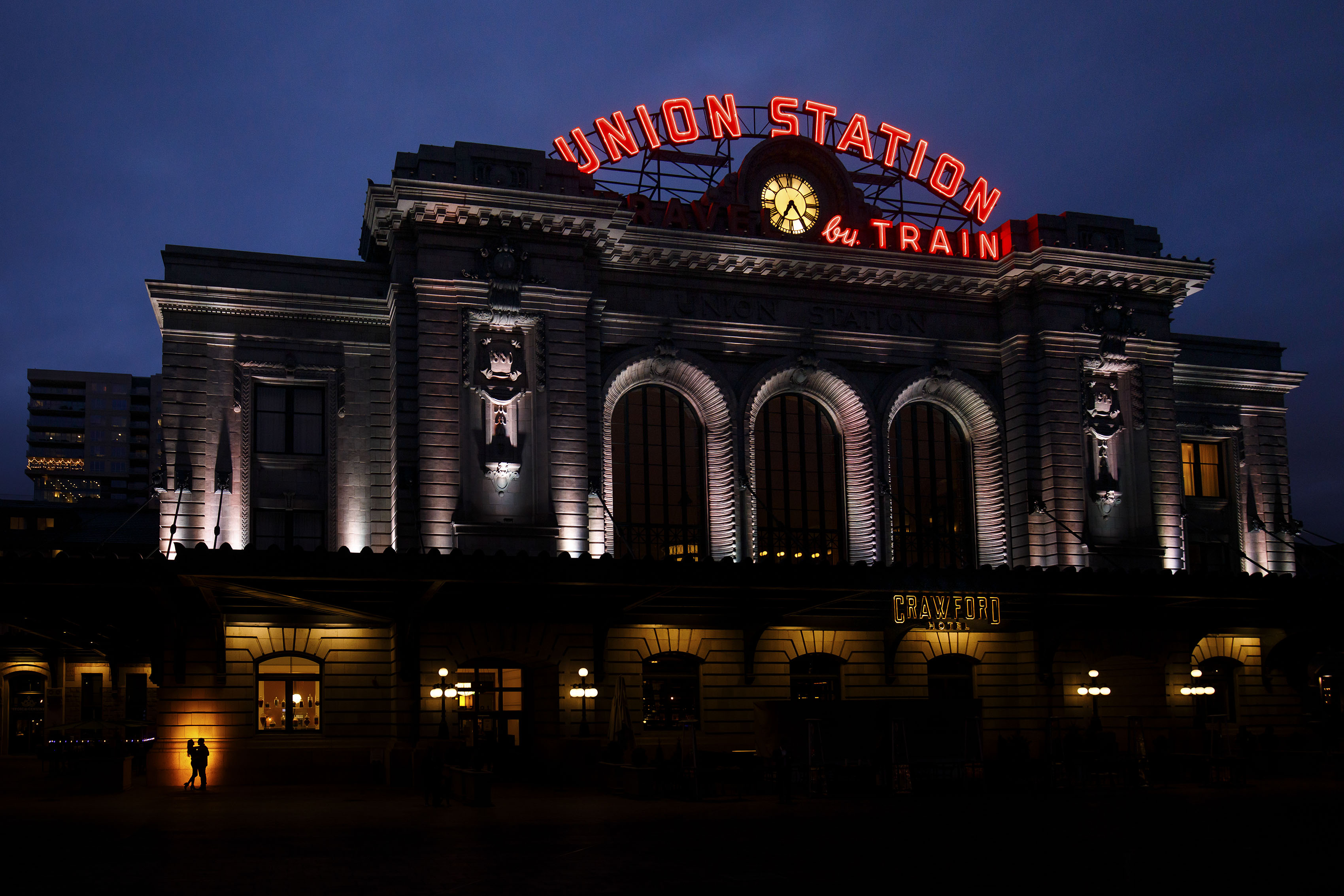 A couple is silhouetted against the building at Denver's Union Station during their engagement photos in lower downtown