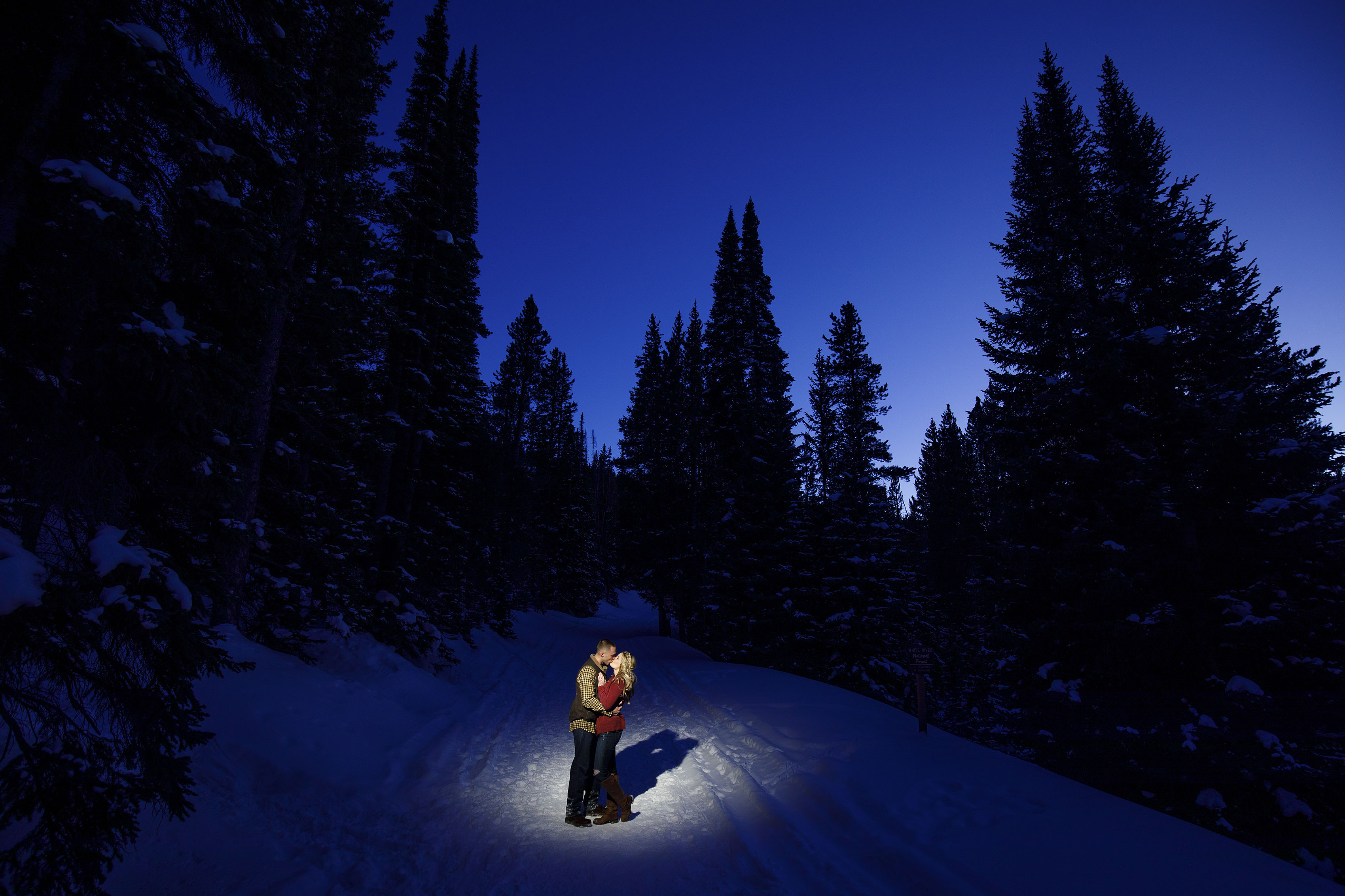 A couple share a kiss along snowy Boreas Pass Road in Breckenridge at twilight during a winter engagement session