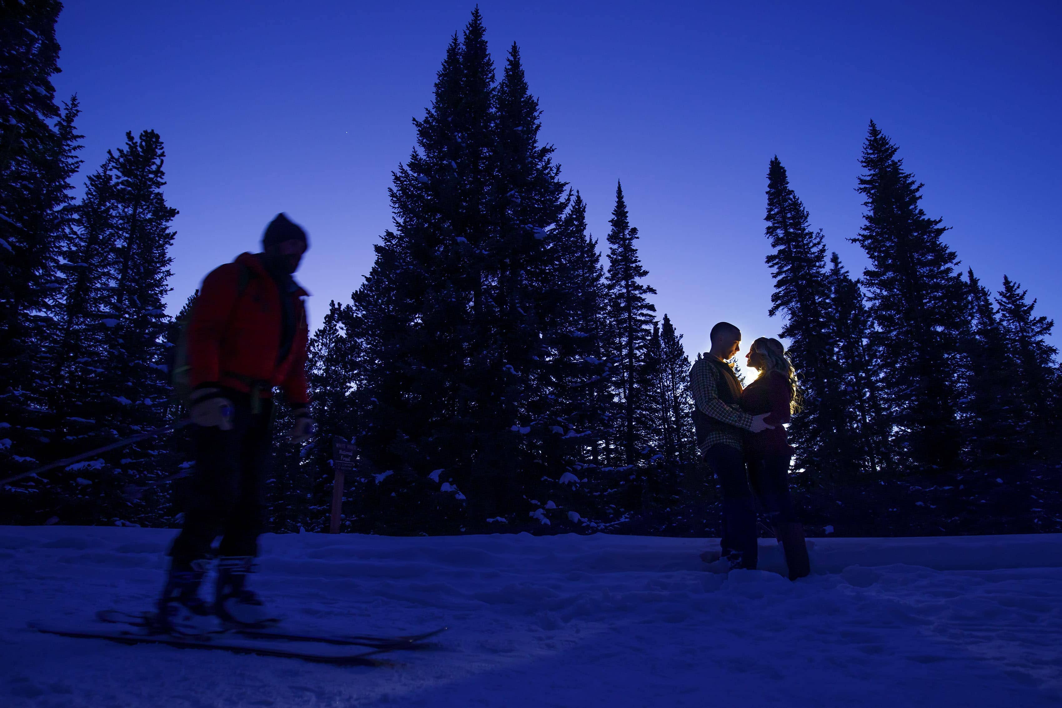 A skier skies past a couple as they embrace on Boreas Pass Road during their winter engagement photos
