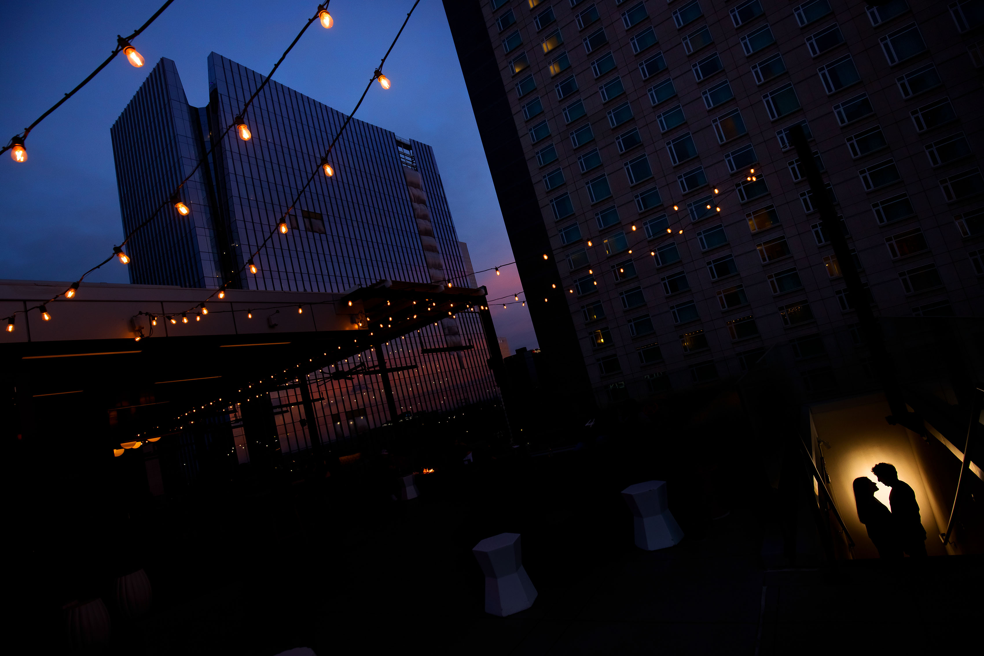 A couple is silhouetted under the market lights at sunset on top at 54thirty rooftop bar in Denver