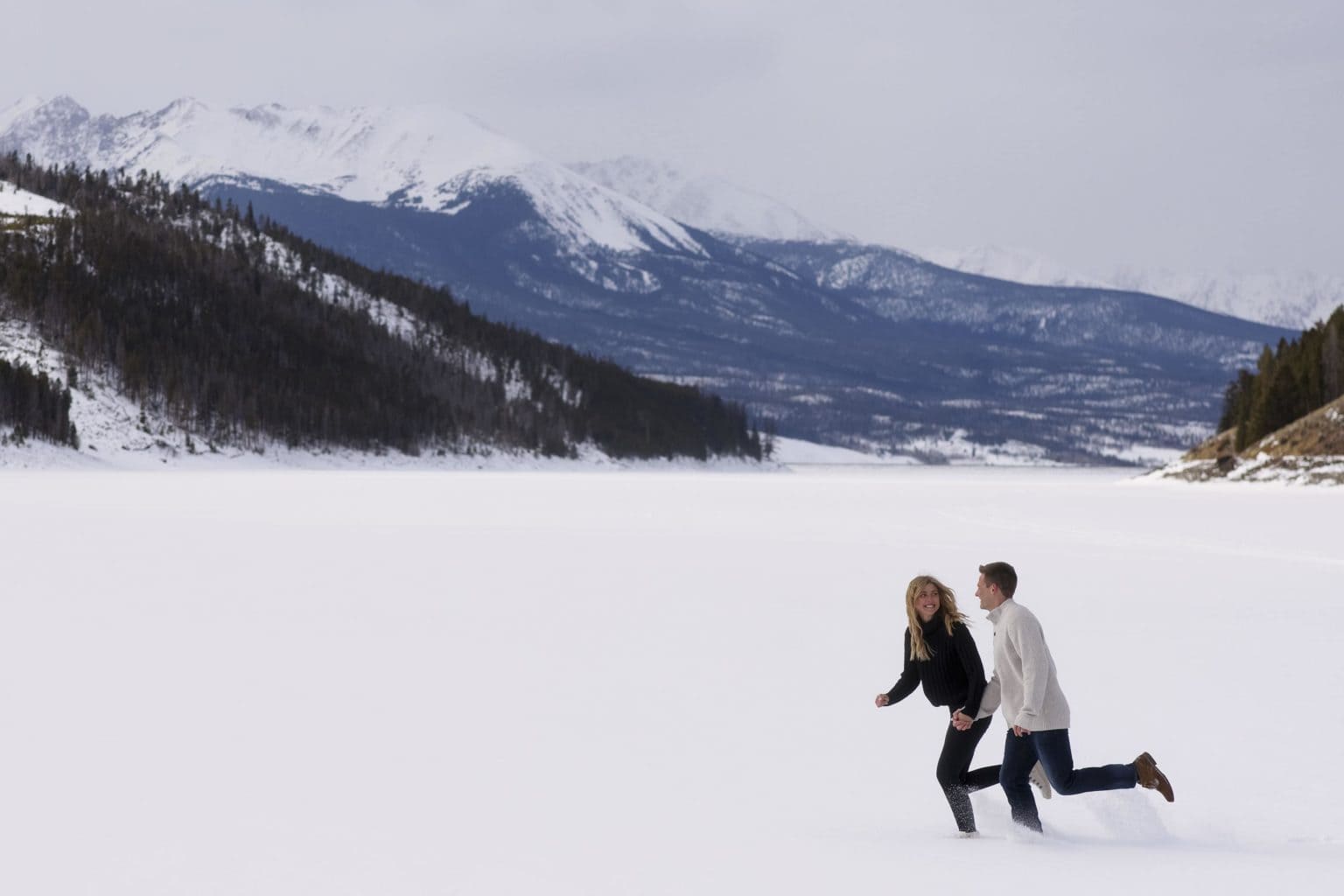 Kayla and Scott run in the snow on frozen Lake Dillon during their engagement photos