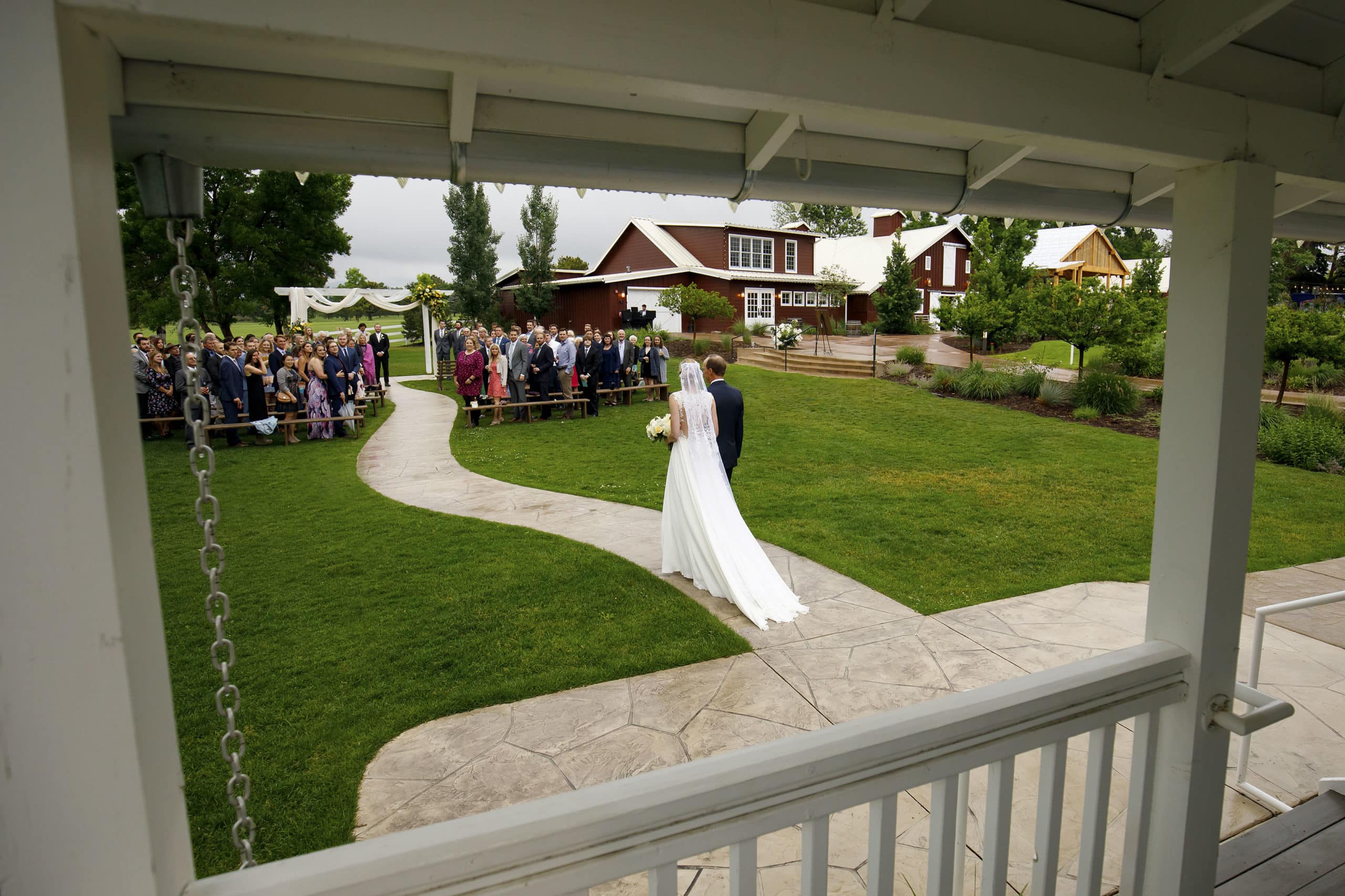 The bride walks down the aisle with her father at the barn at raccoon creek in littleton