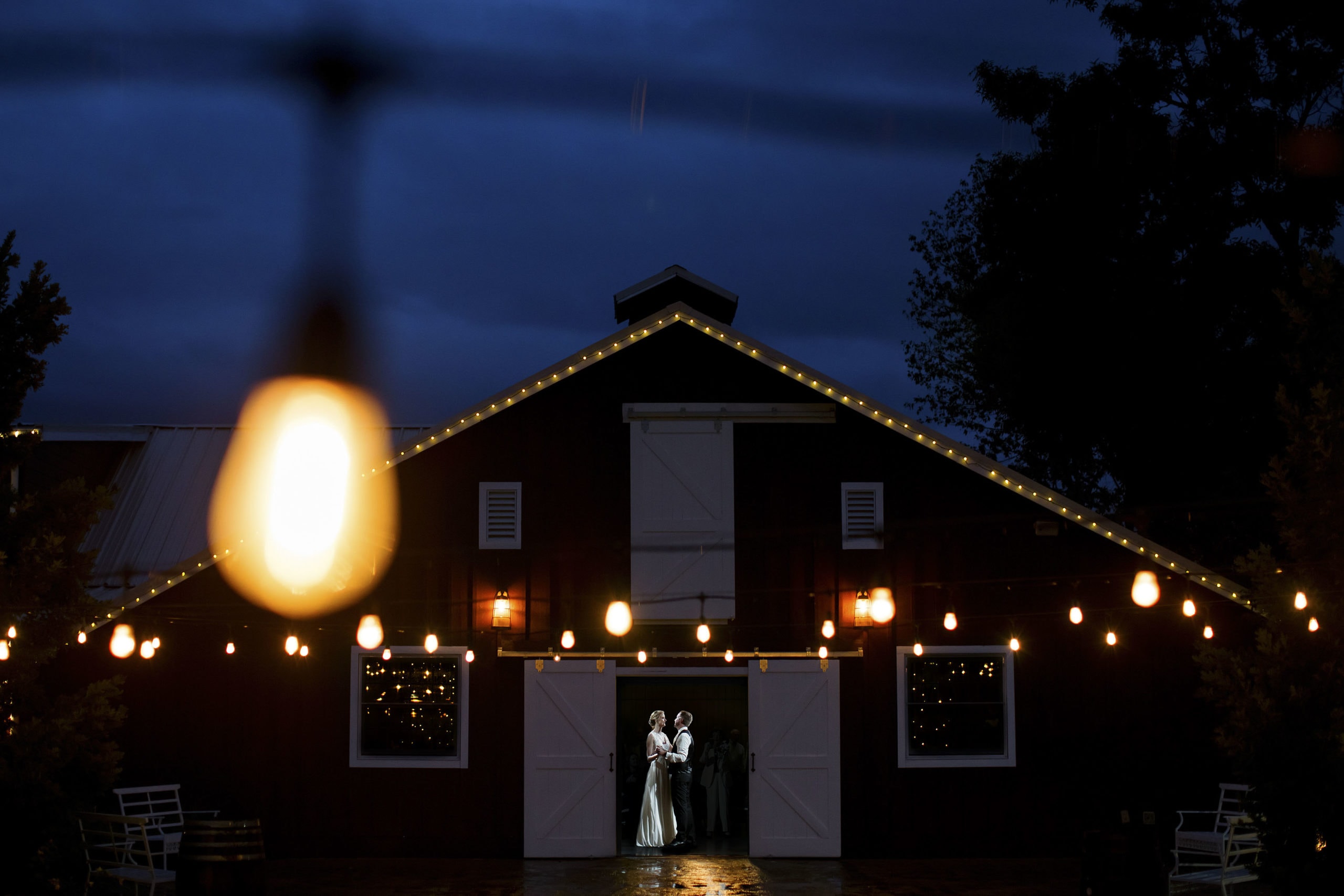the bride and groom share their first dance at the wedding reception during twilight as market lights shine at the barn at raccoon creek