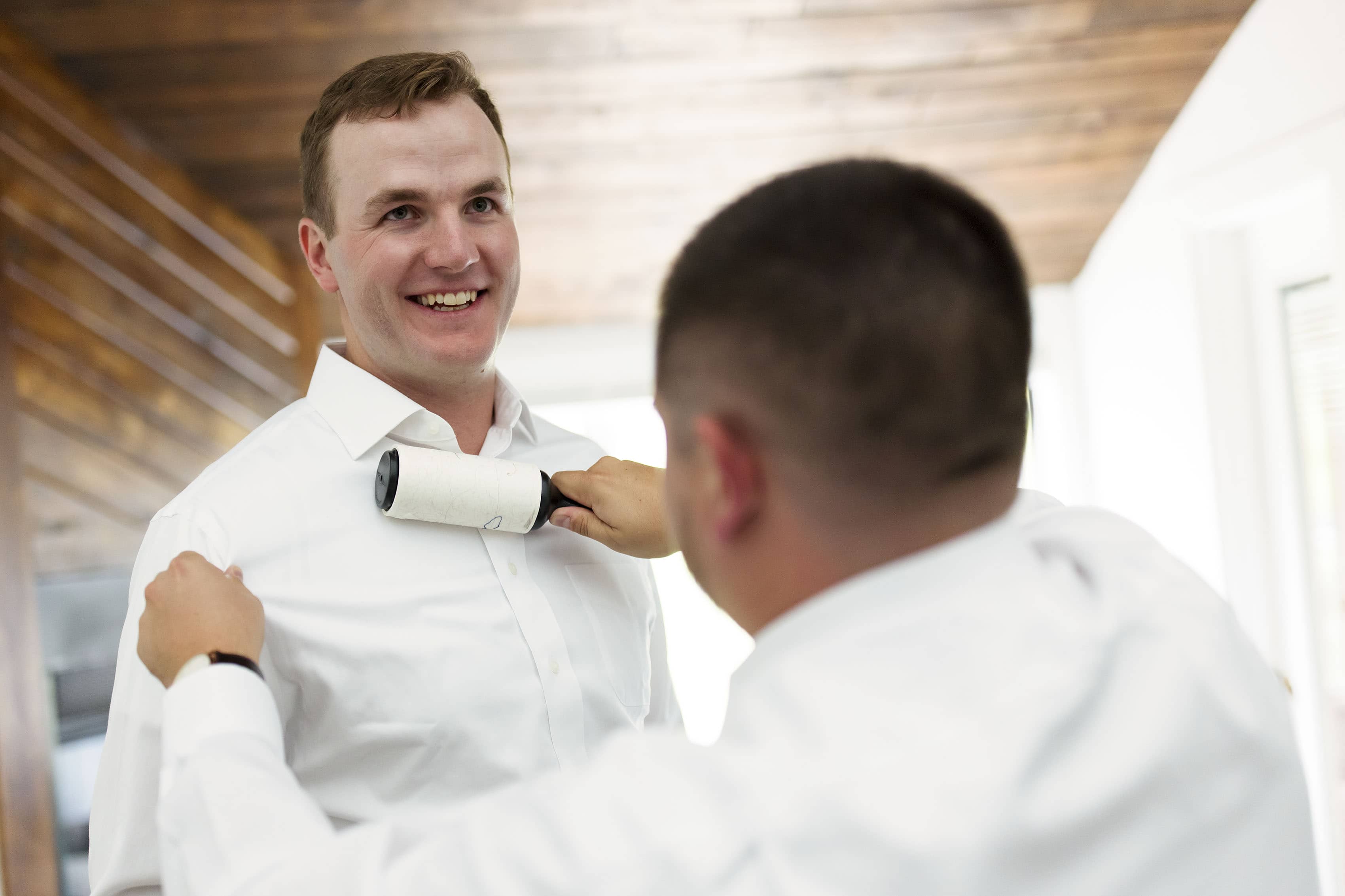 The groom has his lint on his shirt removed by a friend