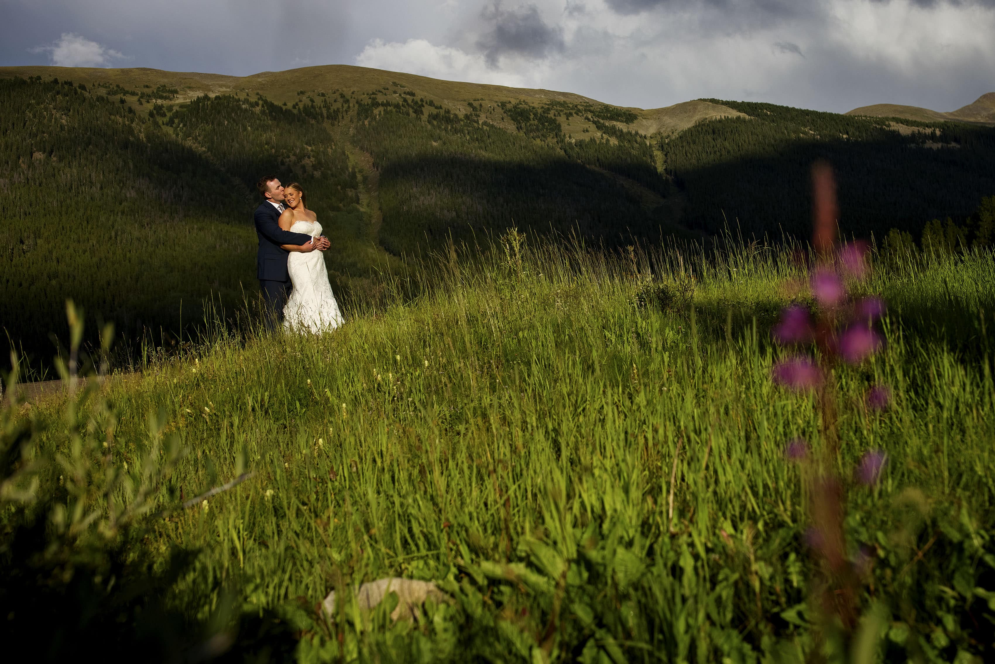 The groom kisses the bride on her forehead as they embrace on a hill near the Tenmile range during their Copper Mountain wedding