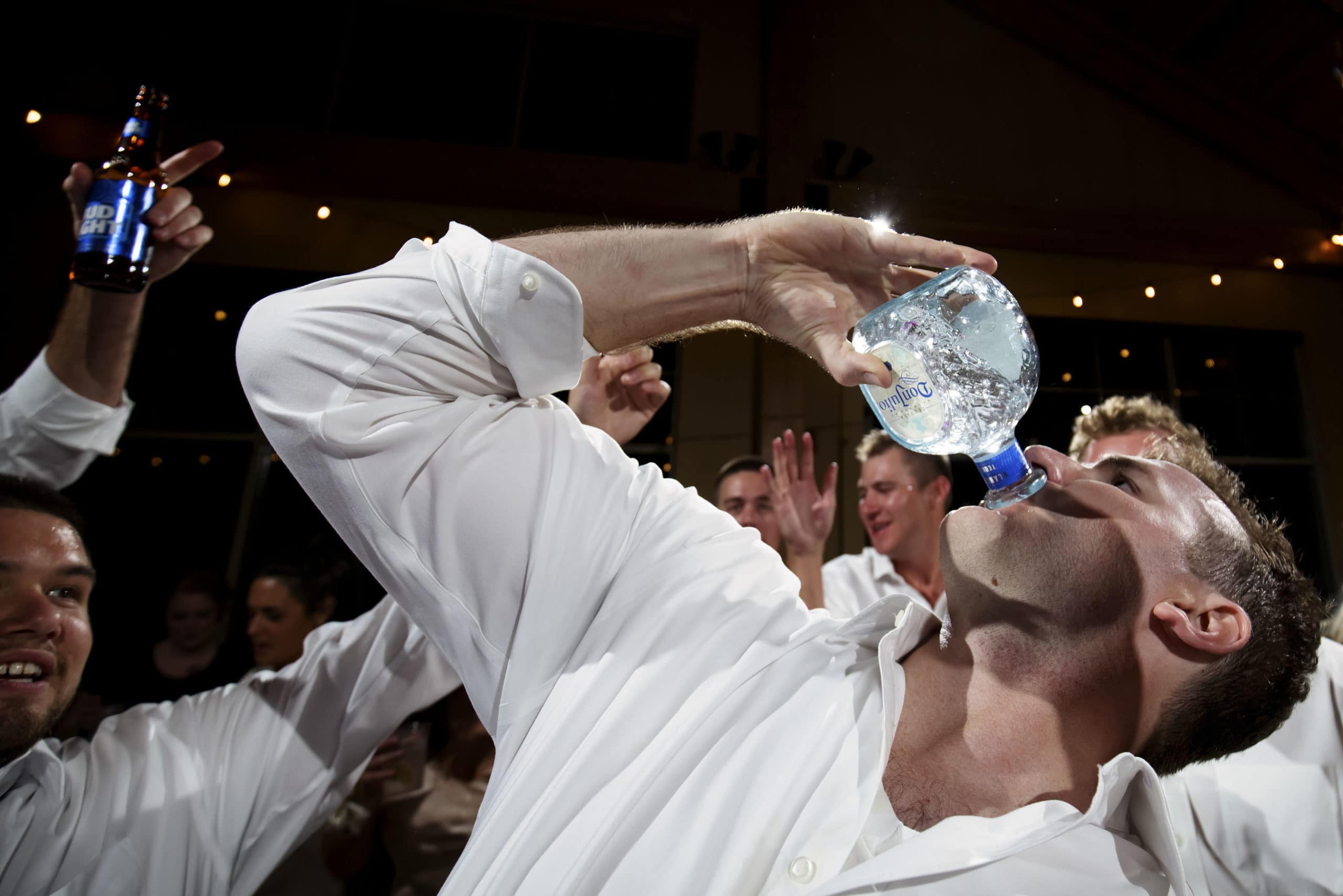 The groom drinks from a bottle of tequila during his wedding reception in the Grand Hall at Copper Station