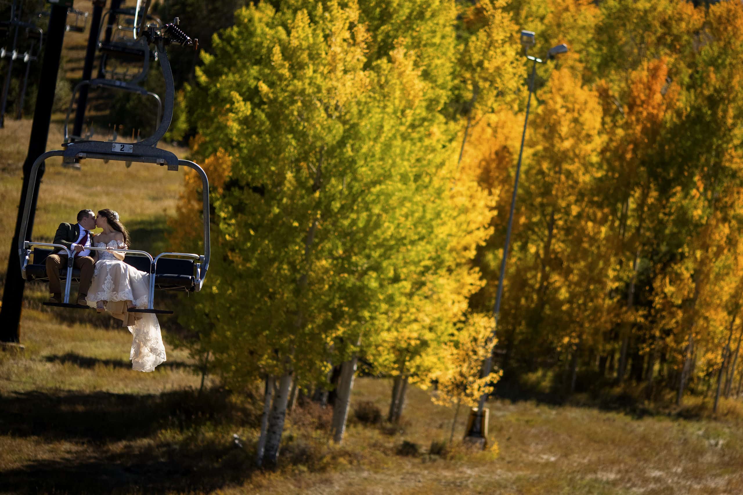 The bride and groom share a kiss on the Quick Draw Express chairlift near a grove of colorful aspen trees following their elopement ceremony