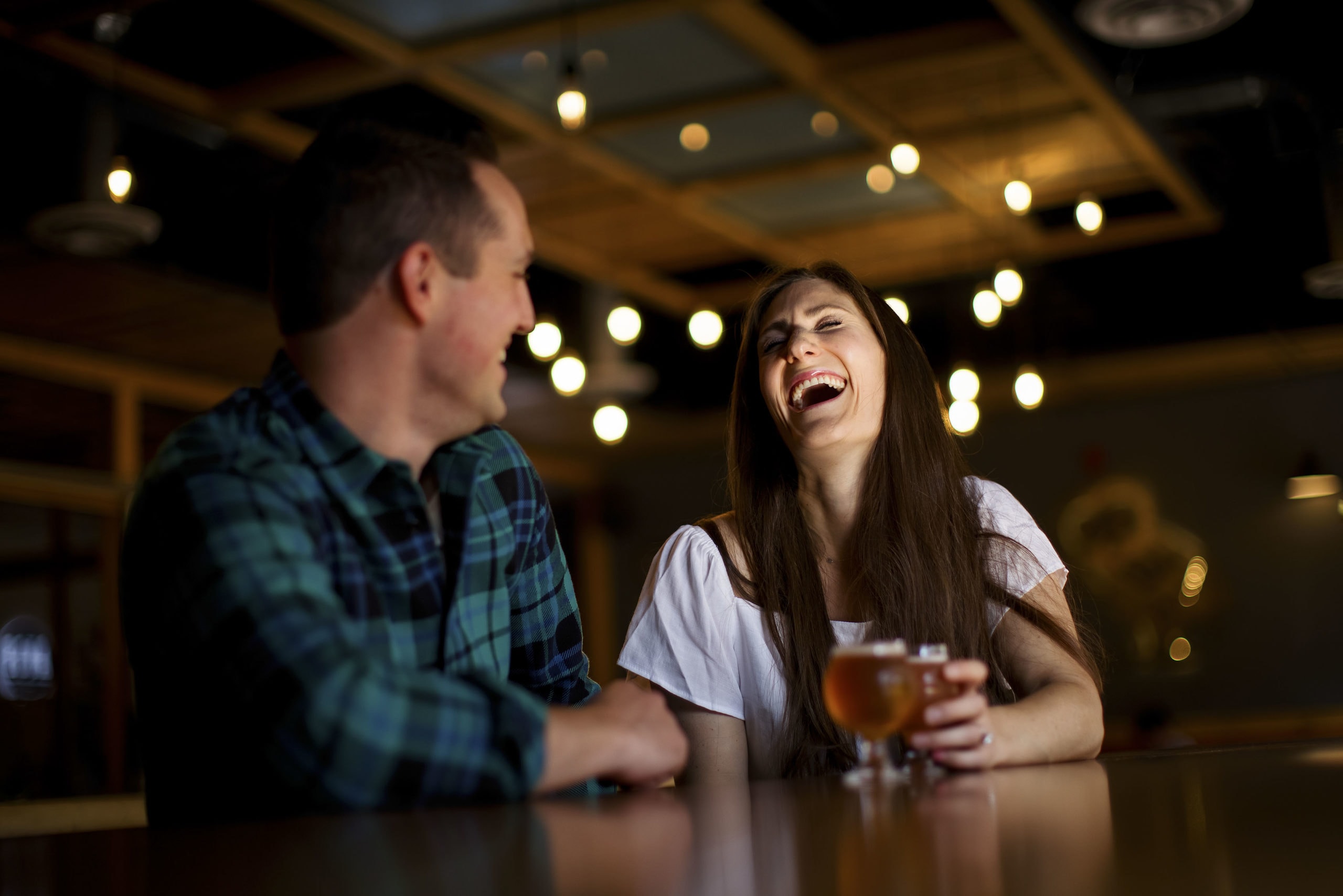 A couple shares a laugh and a beer at Sanitas Brewing during their engagement photos