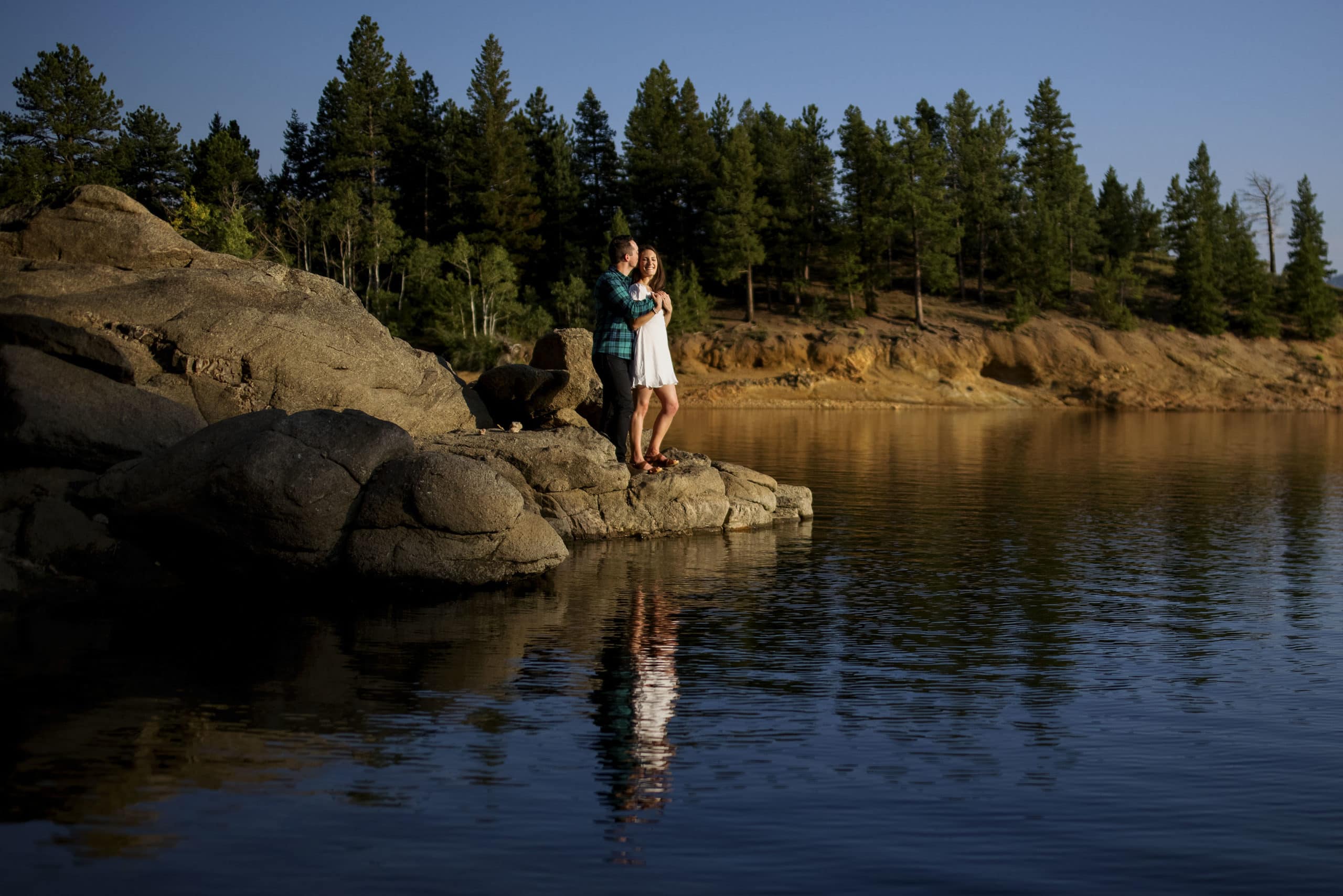 A couple embraces on a rock near Gross Reservoir in Boulder county during their engagement photos
