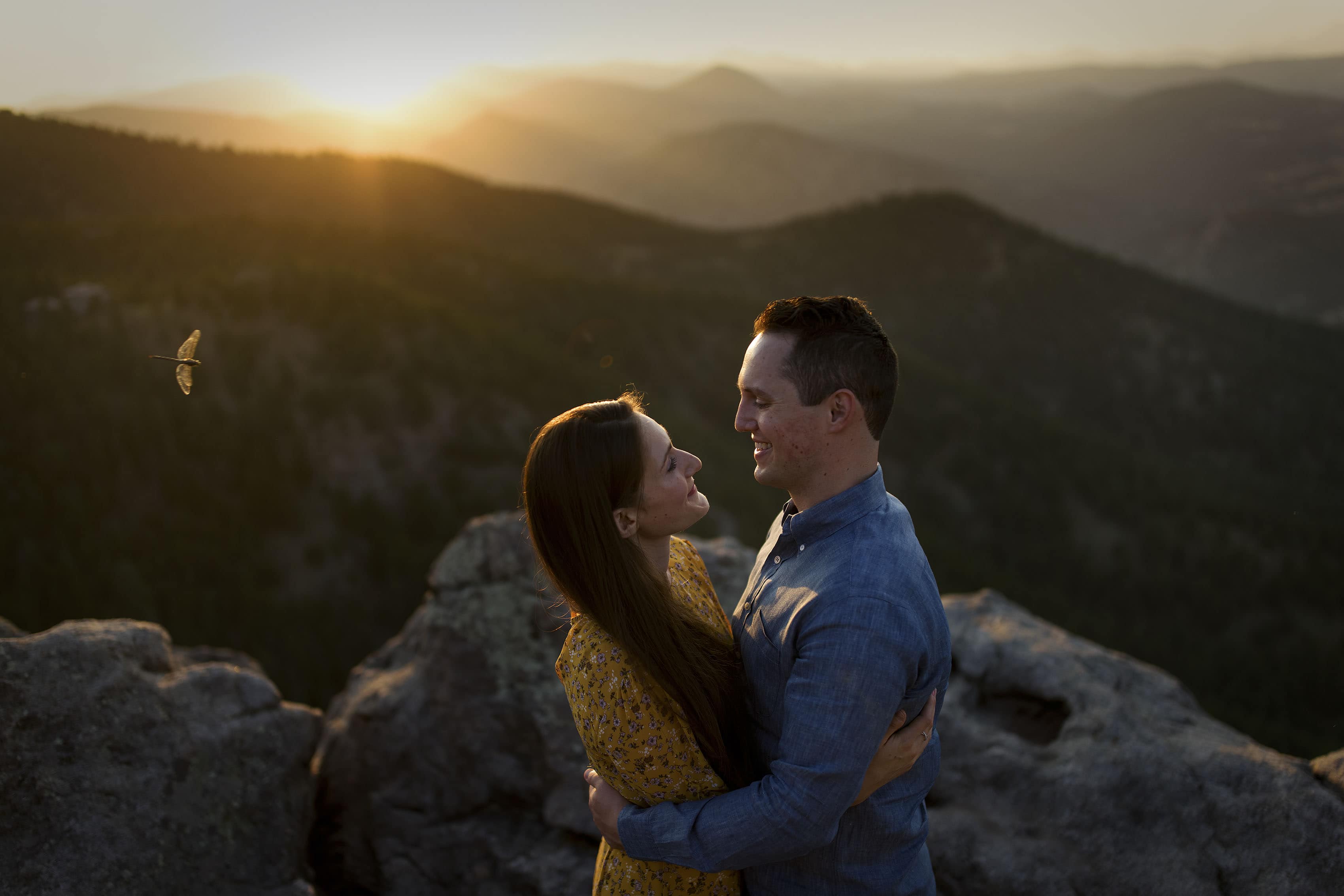 A dragonfly flies by a couple embracing at Lost Gulch Overlook at sunset during their engagement photos