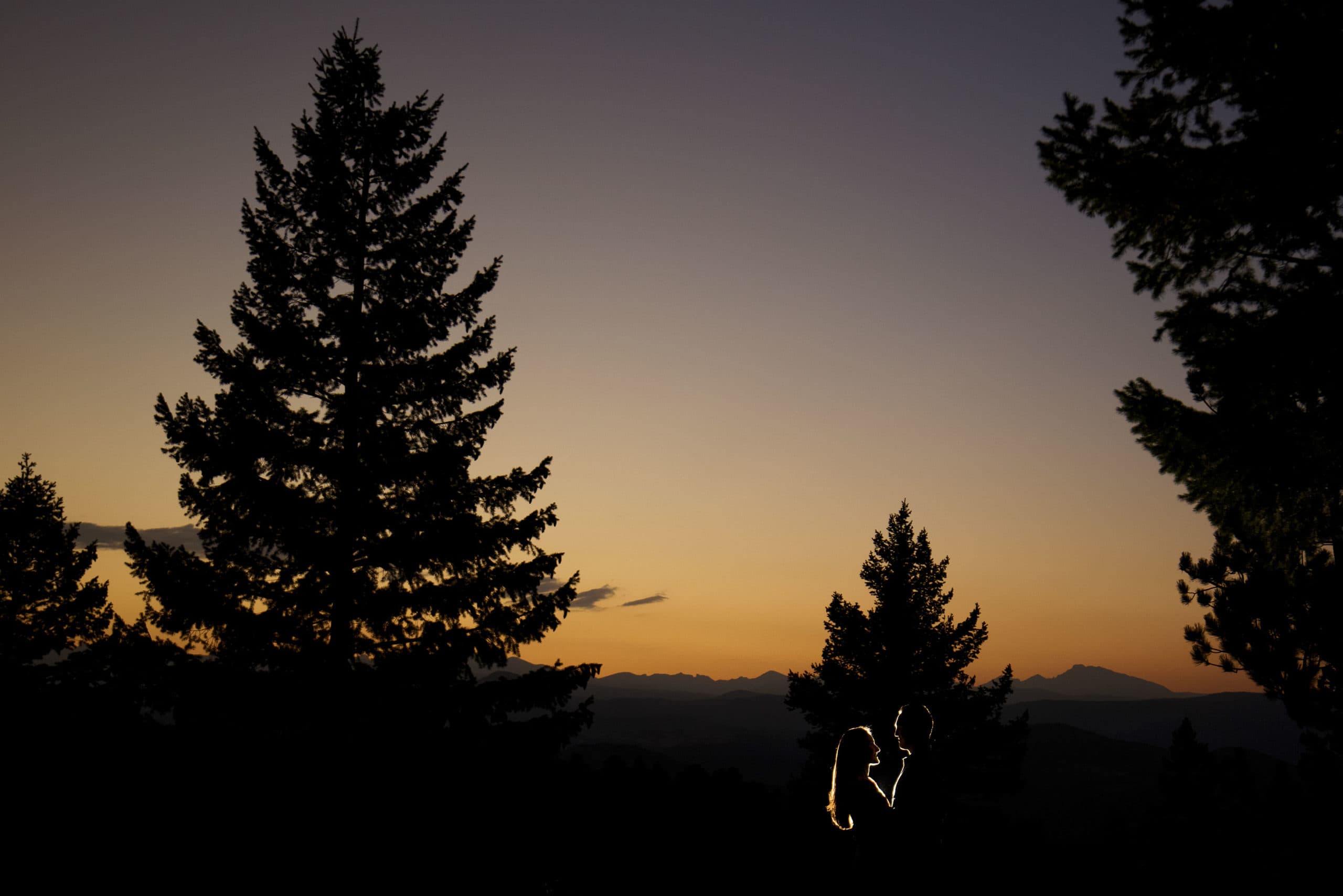 A couple is silhouetted against the sunset in the mountains above Boulder, Colorado