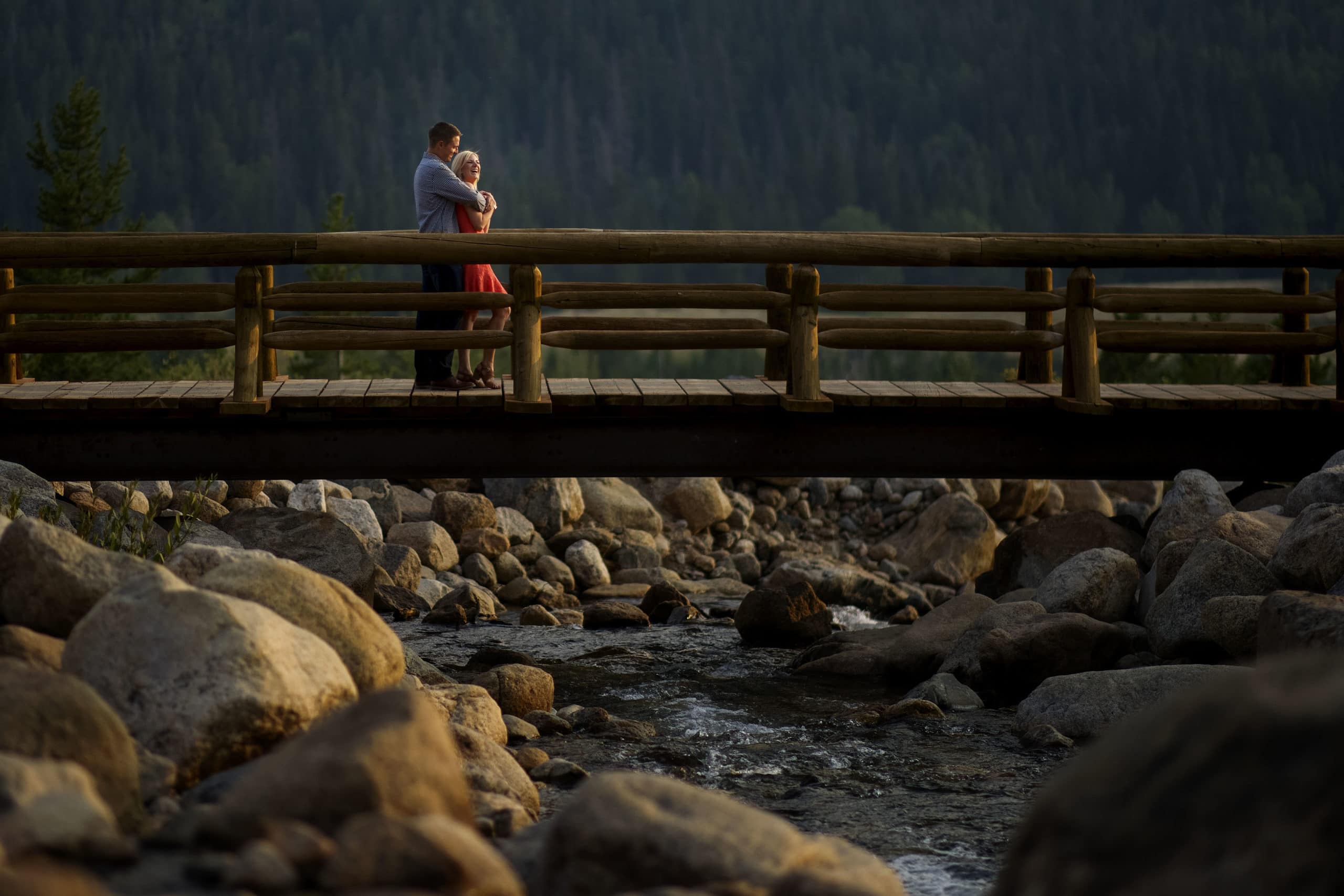 Beth and Riley embrace on the bridge over the river near Alluvial Fan Trail in RMNP