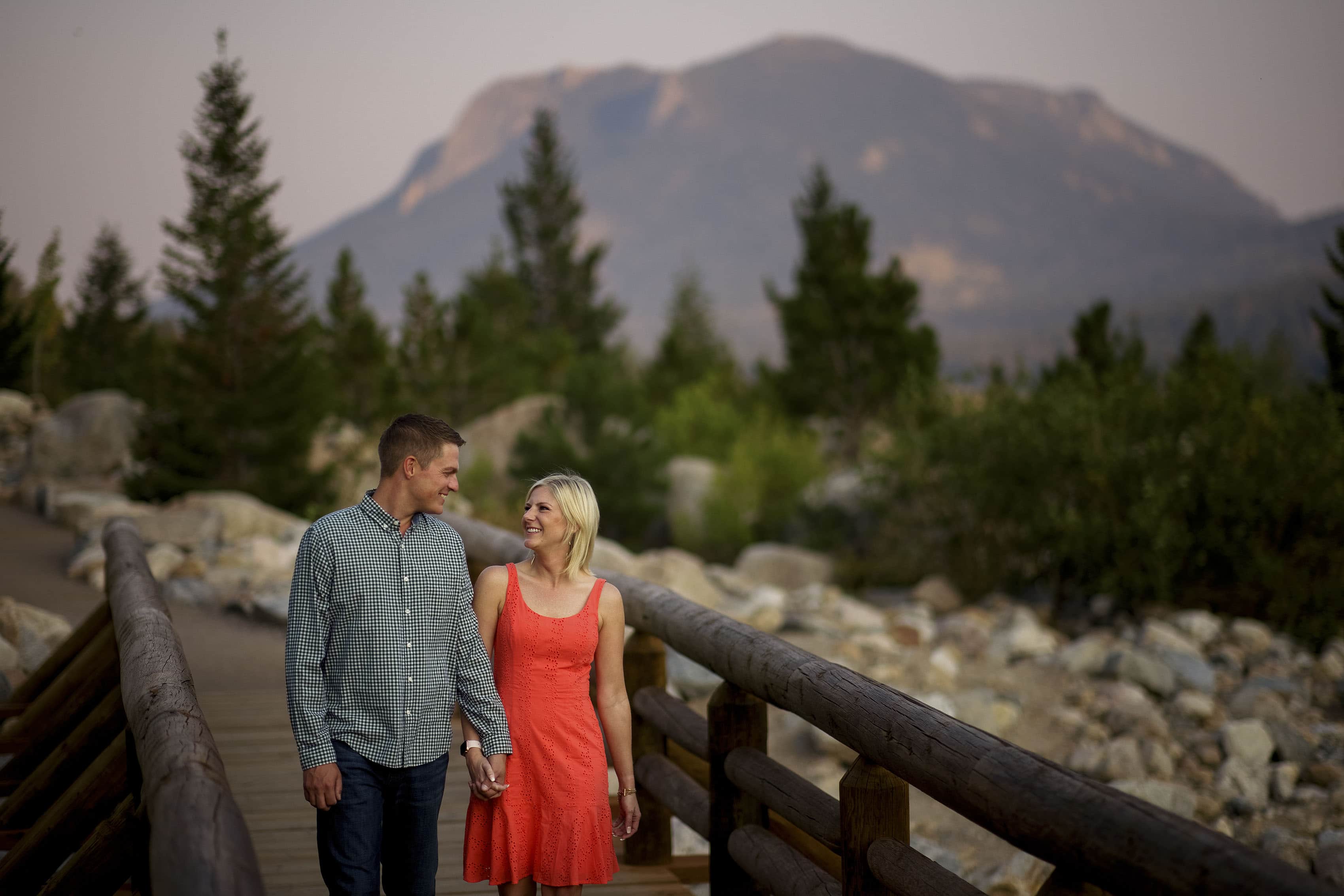 A couple walk along a bridge on the Alluvial Fan Trail during their engagment photos in Rocky Mountain National Park