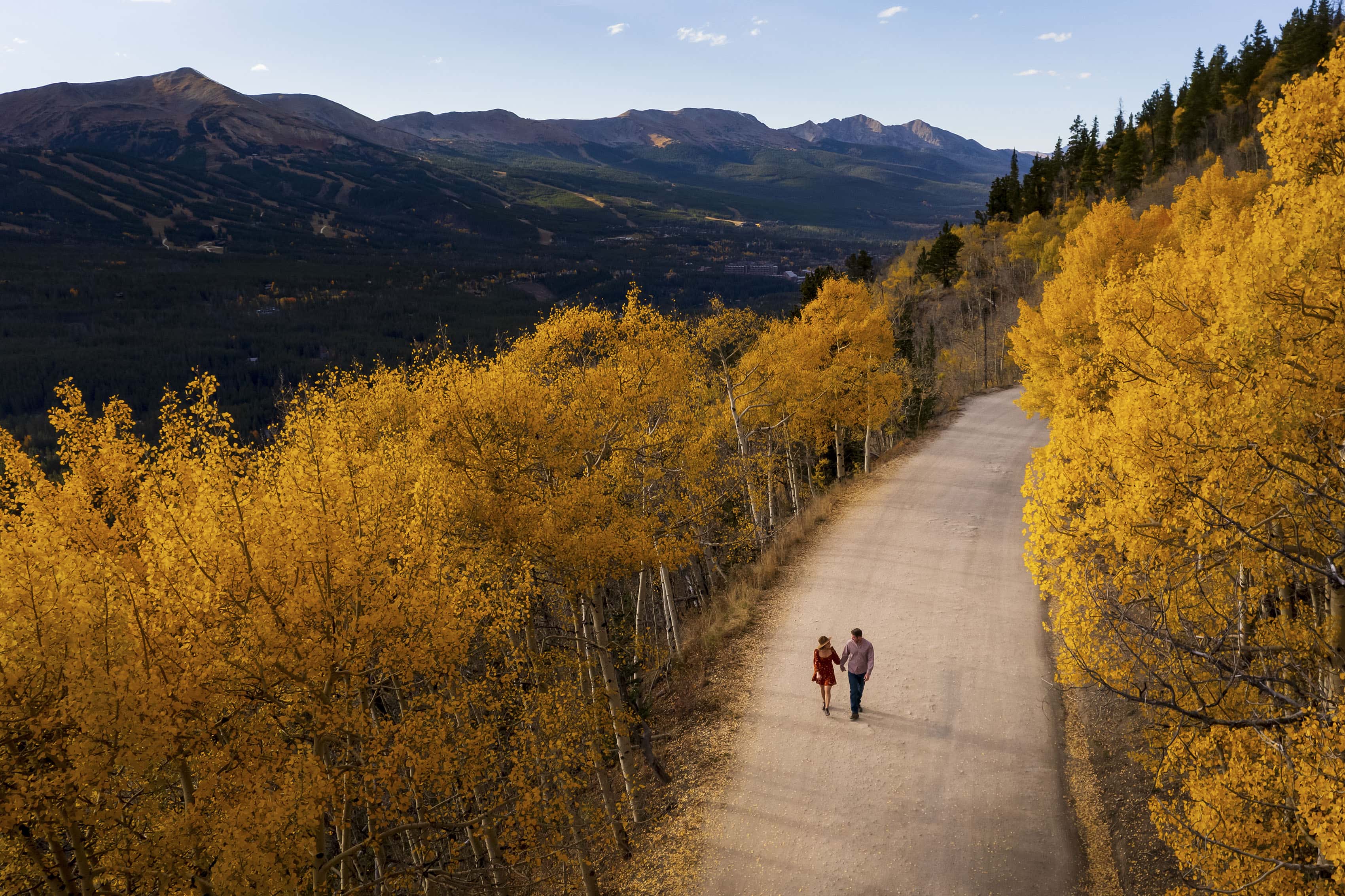 A couple walks along Boreas Pass road, surrounded by yellow aspen trees during their fall engagement photo session in Breckenridge