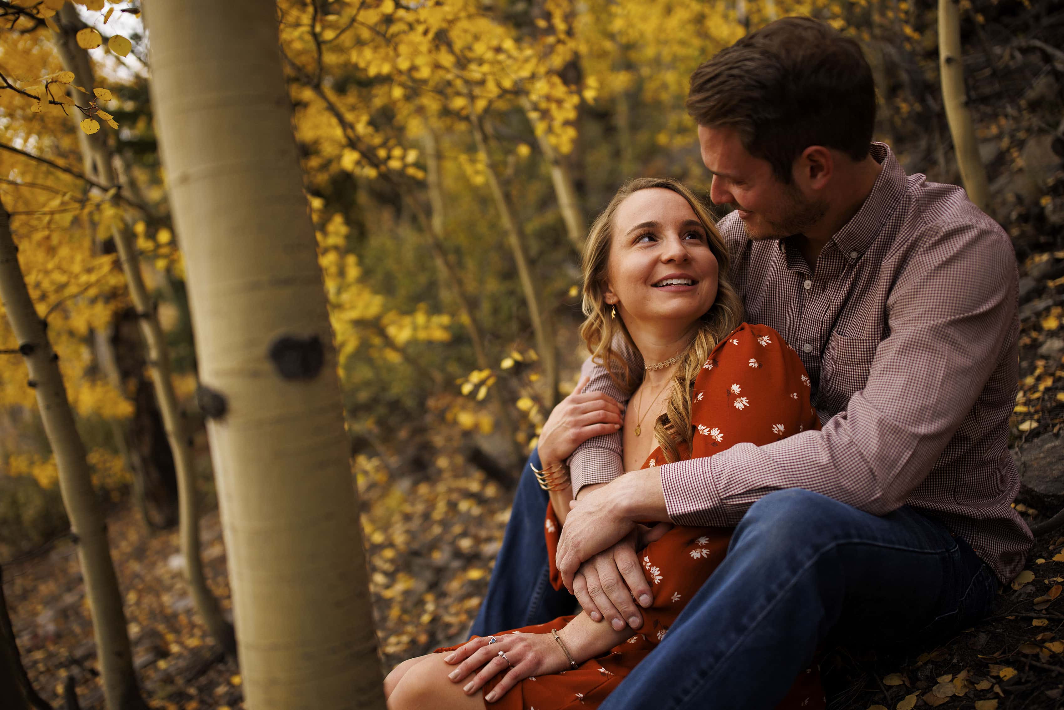 A couple sits on the ground under aspen trees in Breckenridge
