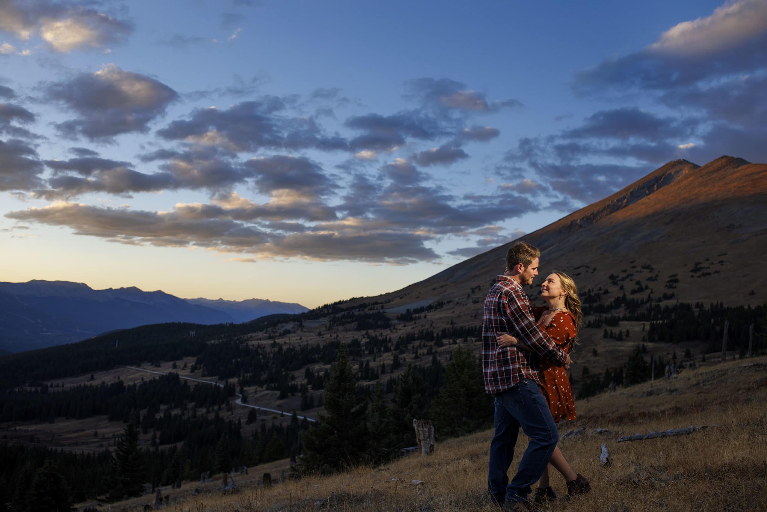 A couple poses on Boreas Pass as the sun sets over the mountains during their engagement photos