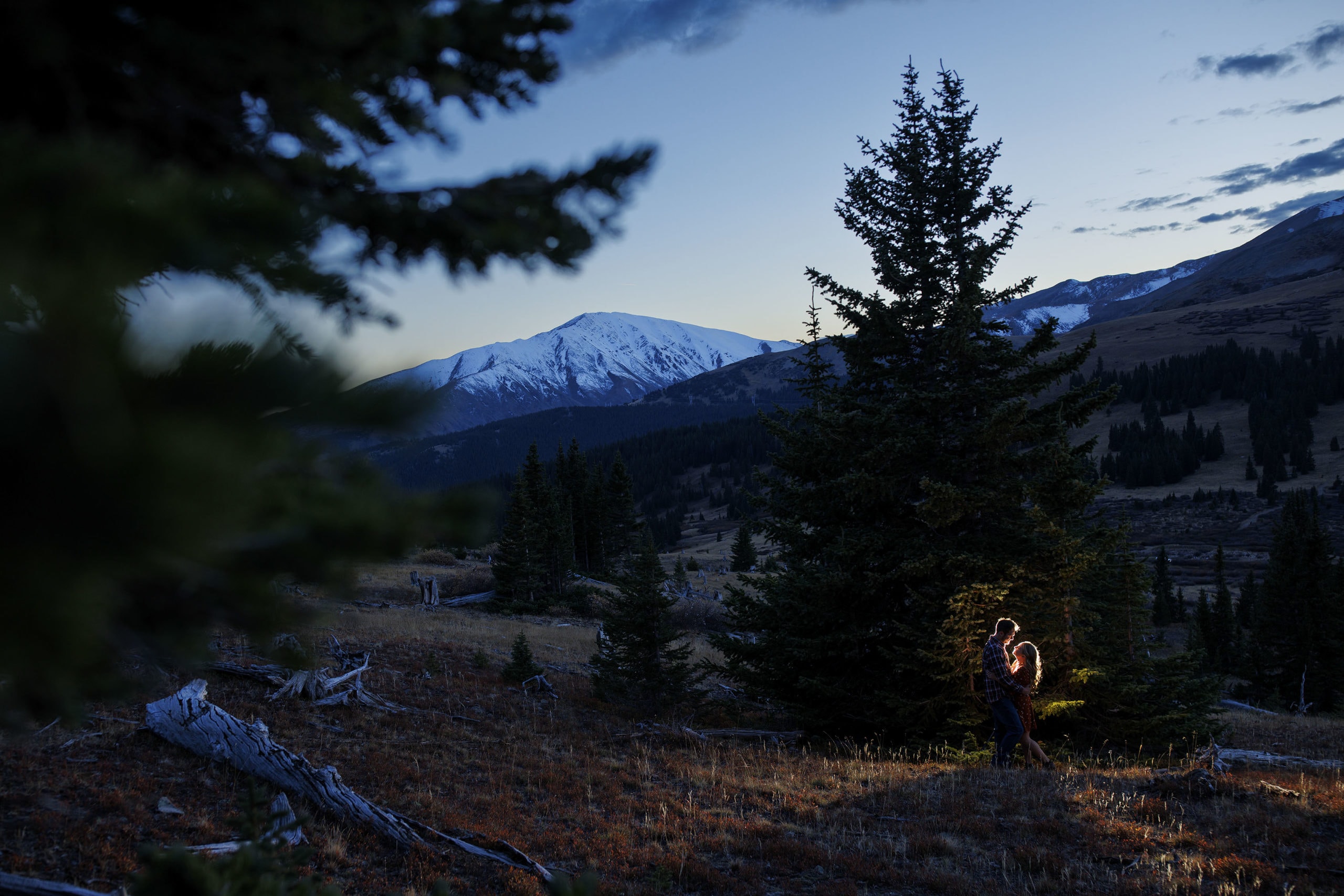 The sun sets over Mt Silverheels as a couple is illuminated against a tree on Boreas Pass during their engagement