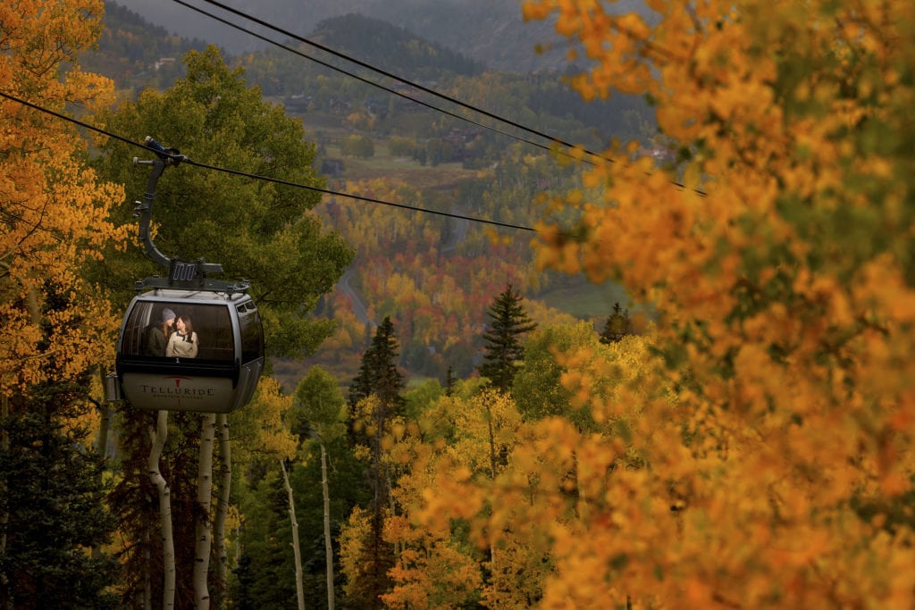 A couple is illuminated in a gondola car, surrounded by colorful aspen trees during their fall colors engagement at Telluride Ski Resort in Colorado