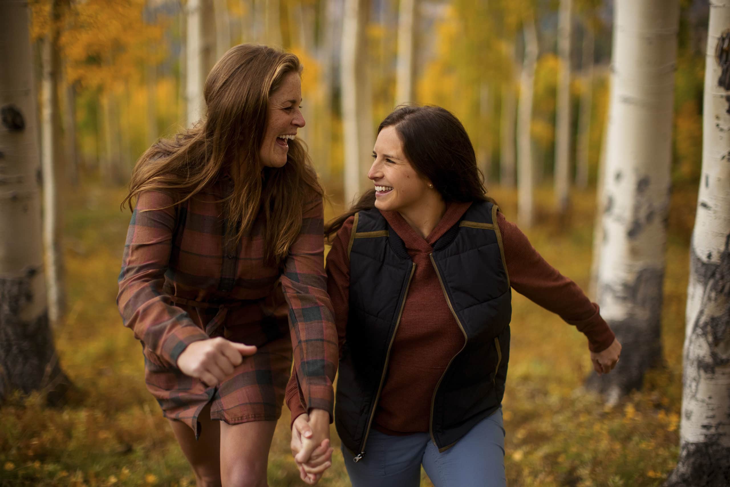 A same sex couple runs together in an aspen grove in Mountain Village, Colorado during their engagement photos