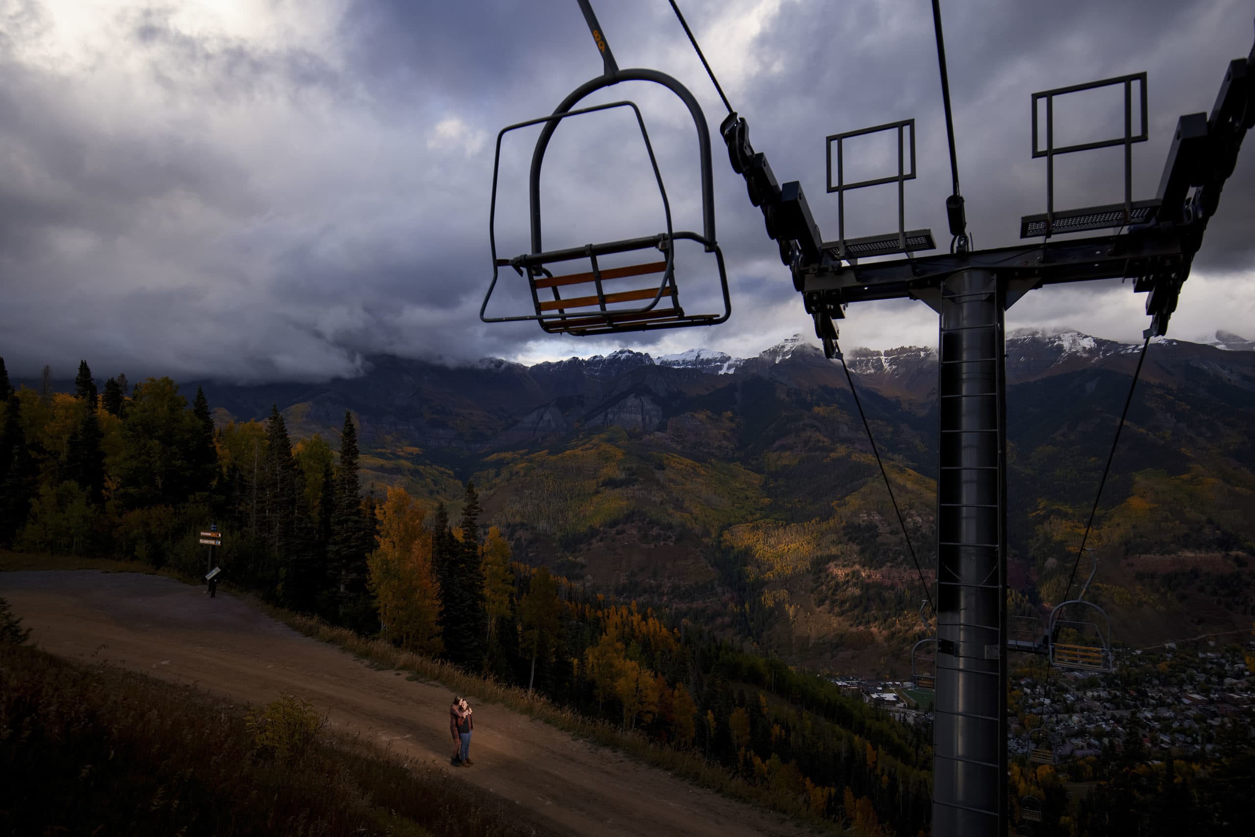 A couple embraces at twilight on Telluride Trail under the Coonskin chairlift during their engagement at Telluride Ski Resort
