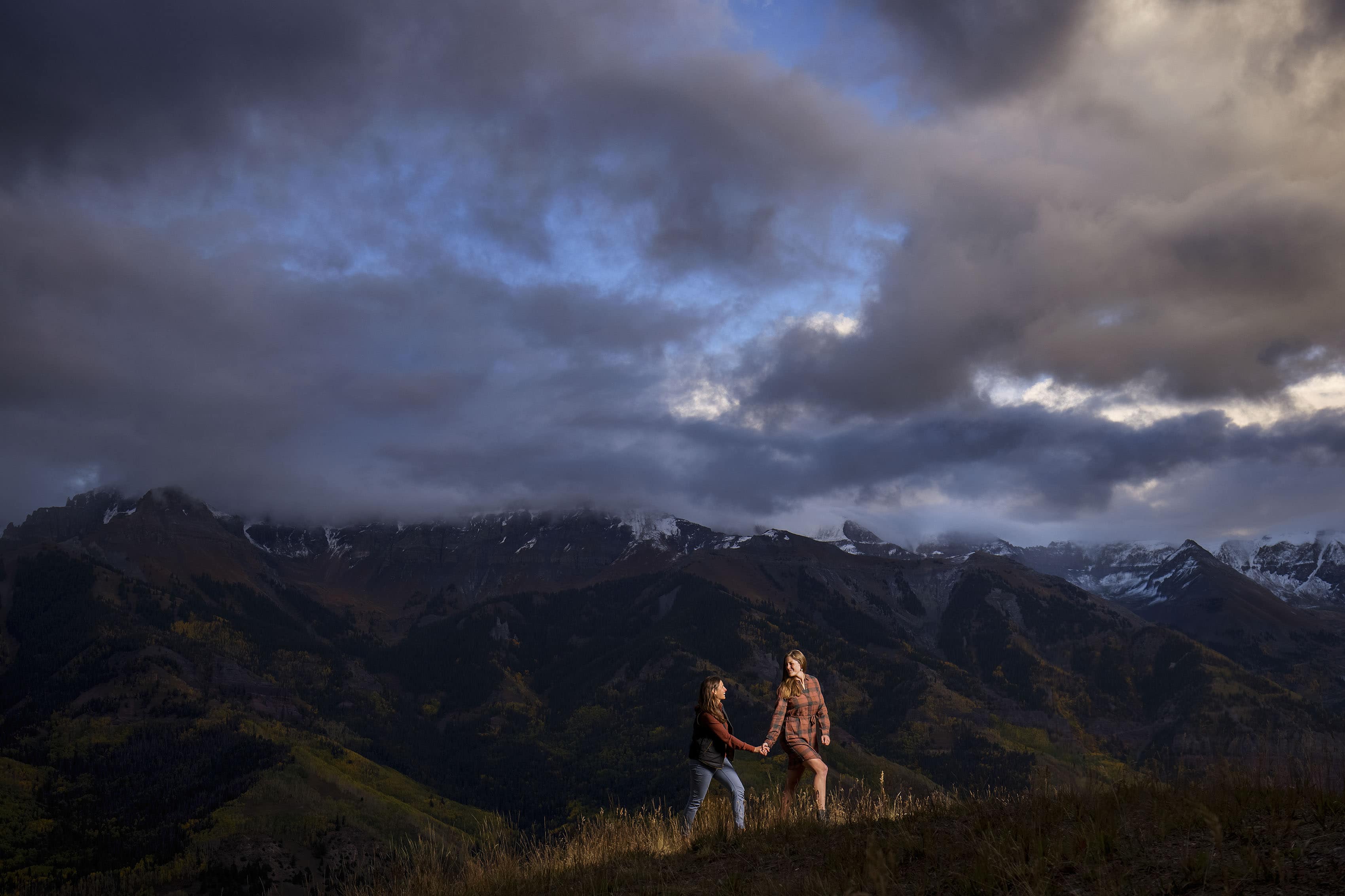 Anna and Cait walk along a ridge near San Sophia Overlook during their fall engagement photos at Telluride Ski Resort
