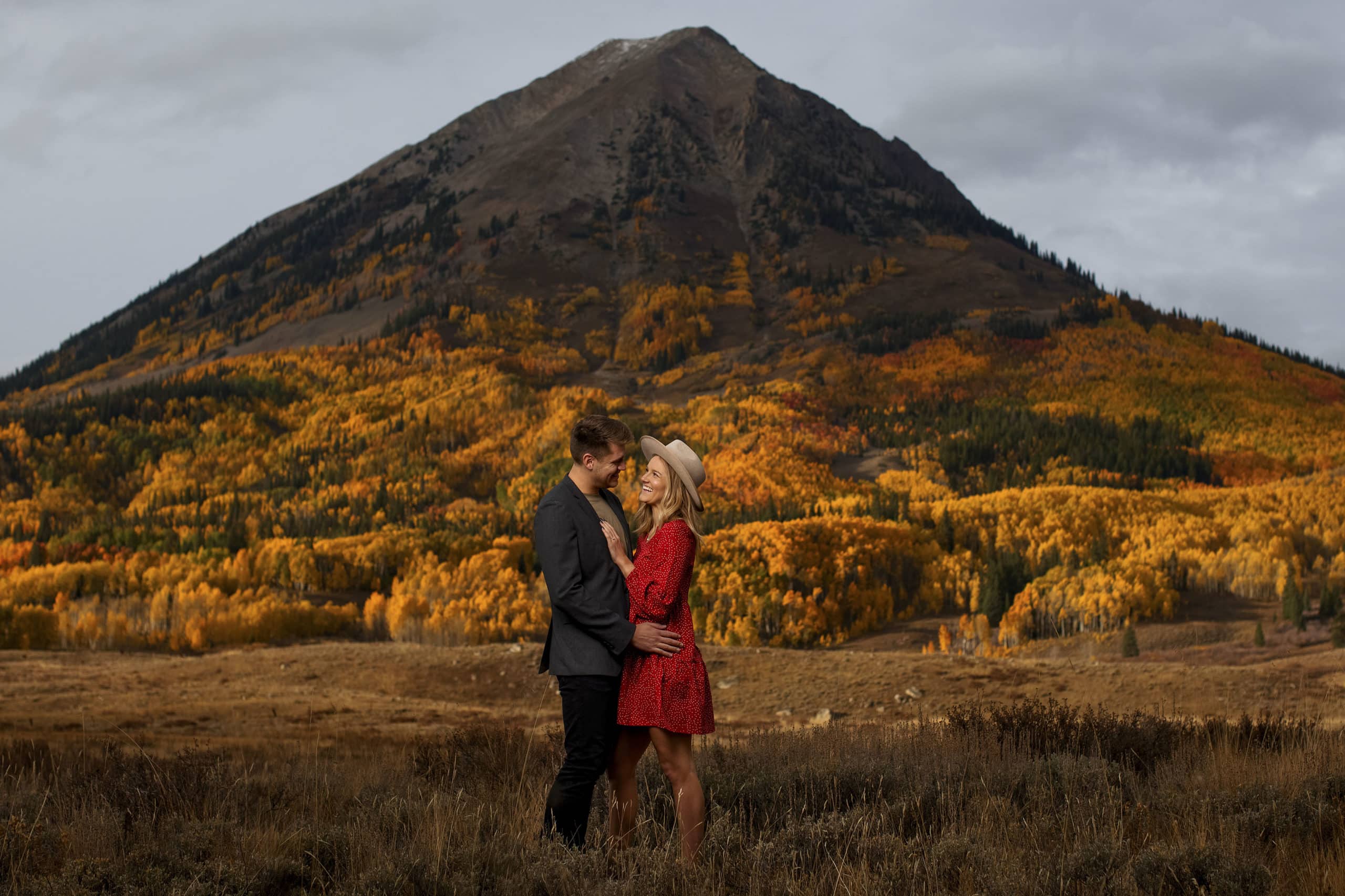 A woman in a red dress and man in a suit pose for a portrait as golden aspen trees glow on Gothic Mountain