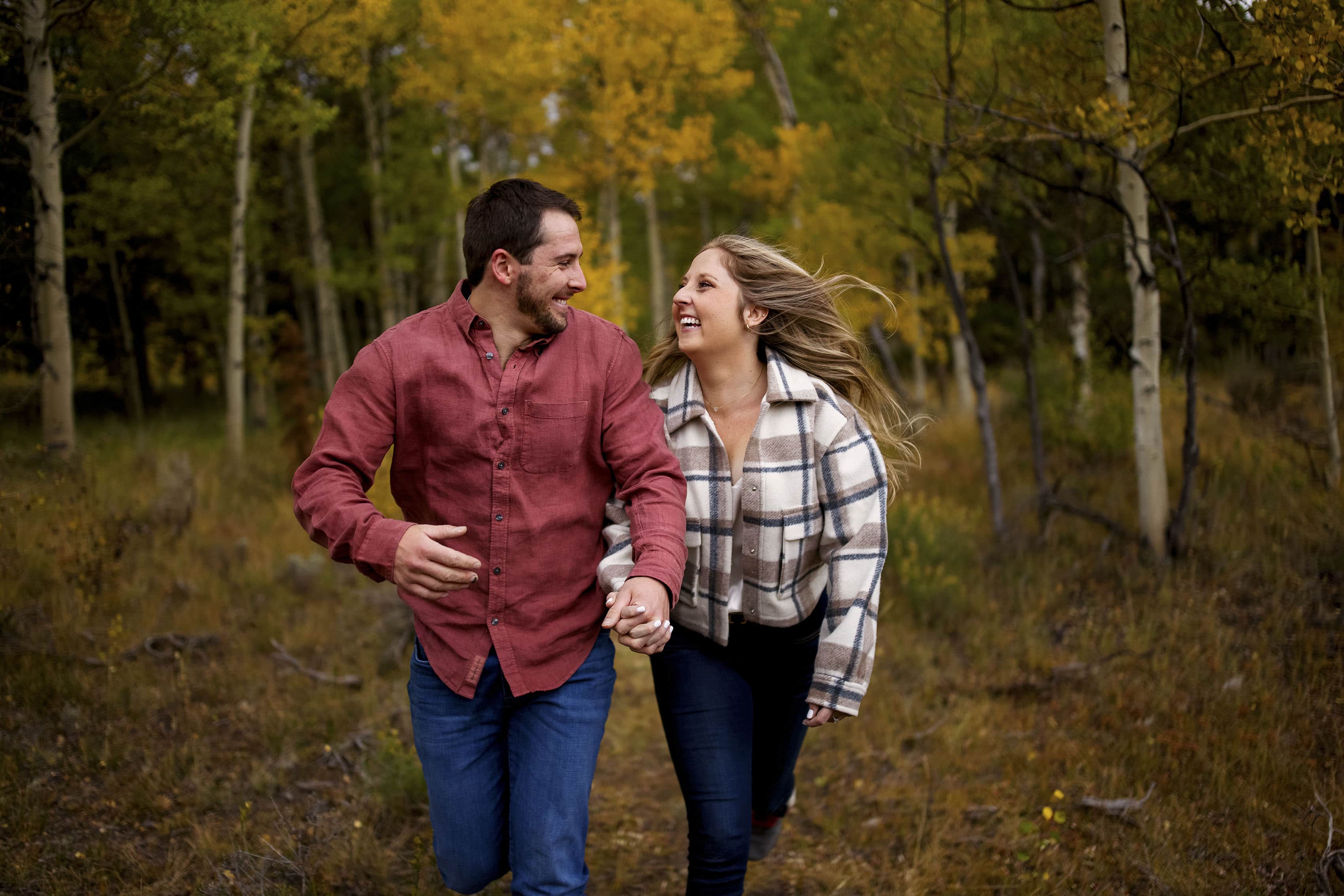 A couple runs in the woods during their engagement photos
