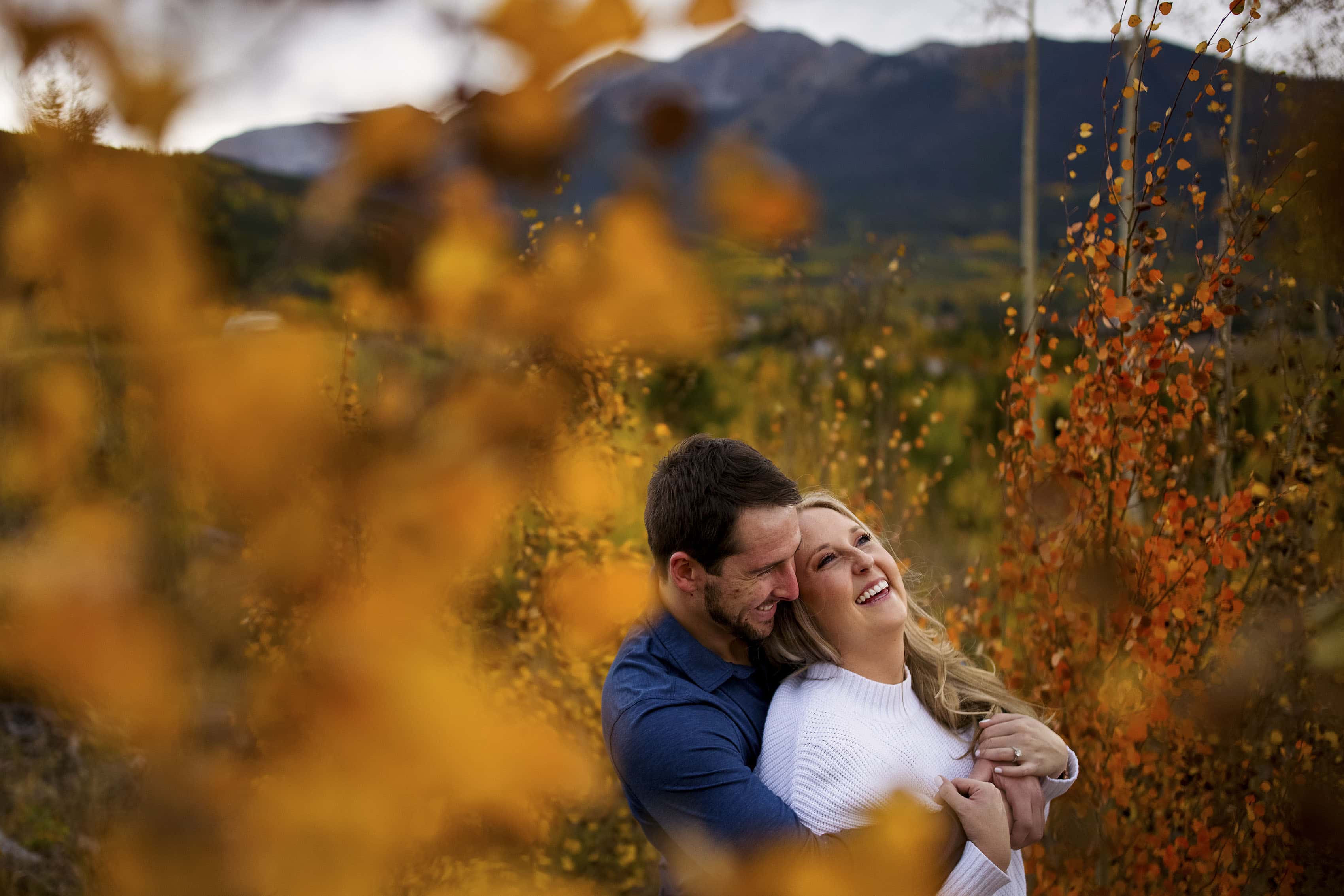A couple embraces near fall colors during their pre-wedding photos in Summit County