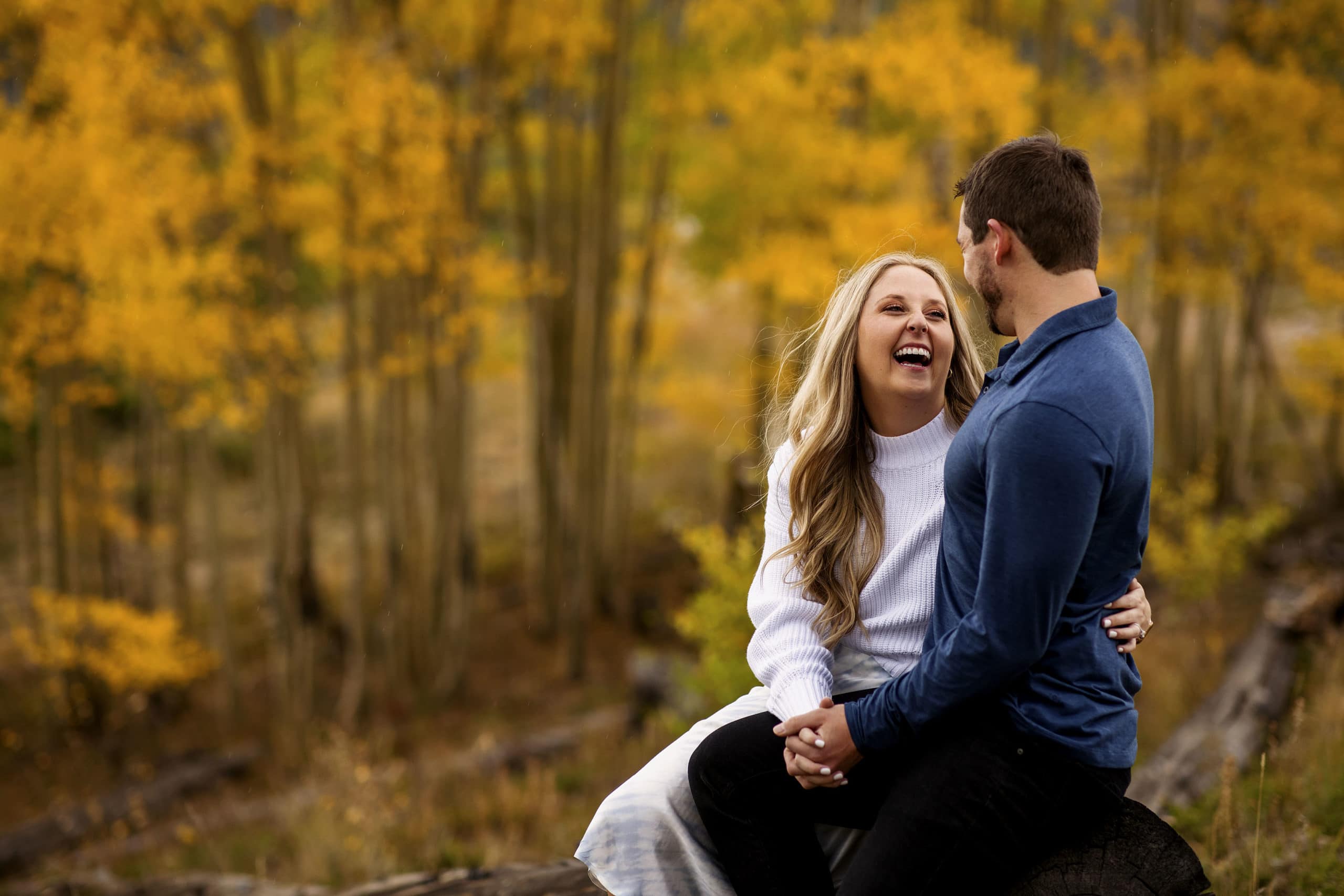 Jamie laughs with Chad as they sit on a log during their engagement photos in Summit County