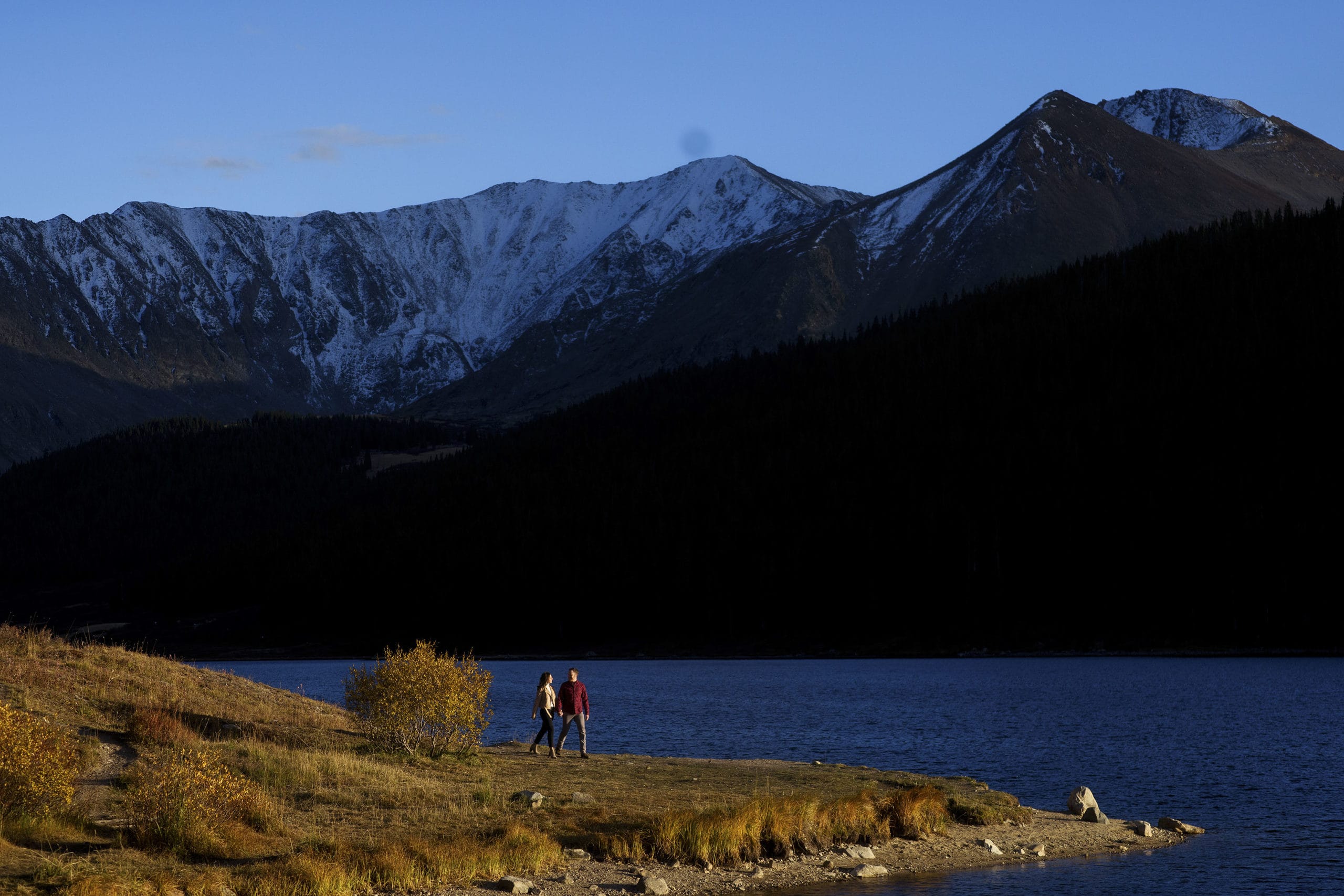 A couple walks on a peninsula at Clinton Gulch Dam Reservoir near Leadville, Colorado during their engagement photos