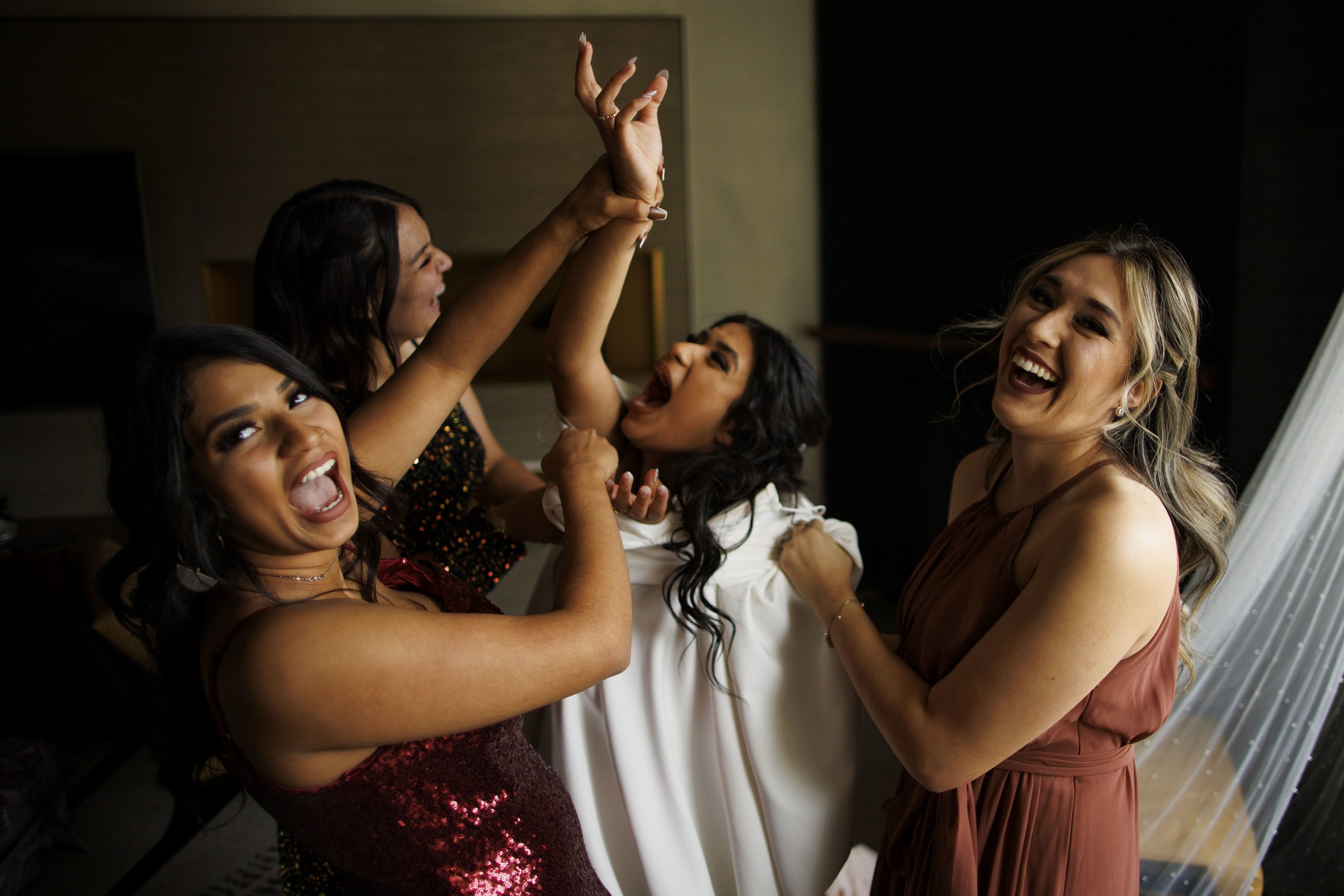 The bride laughs with friends while getting into her wedding dress