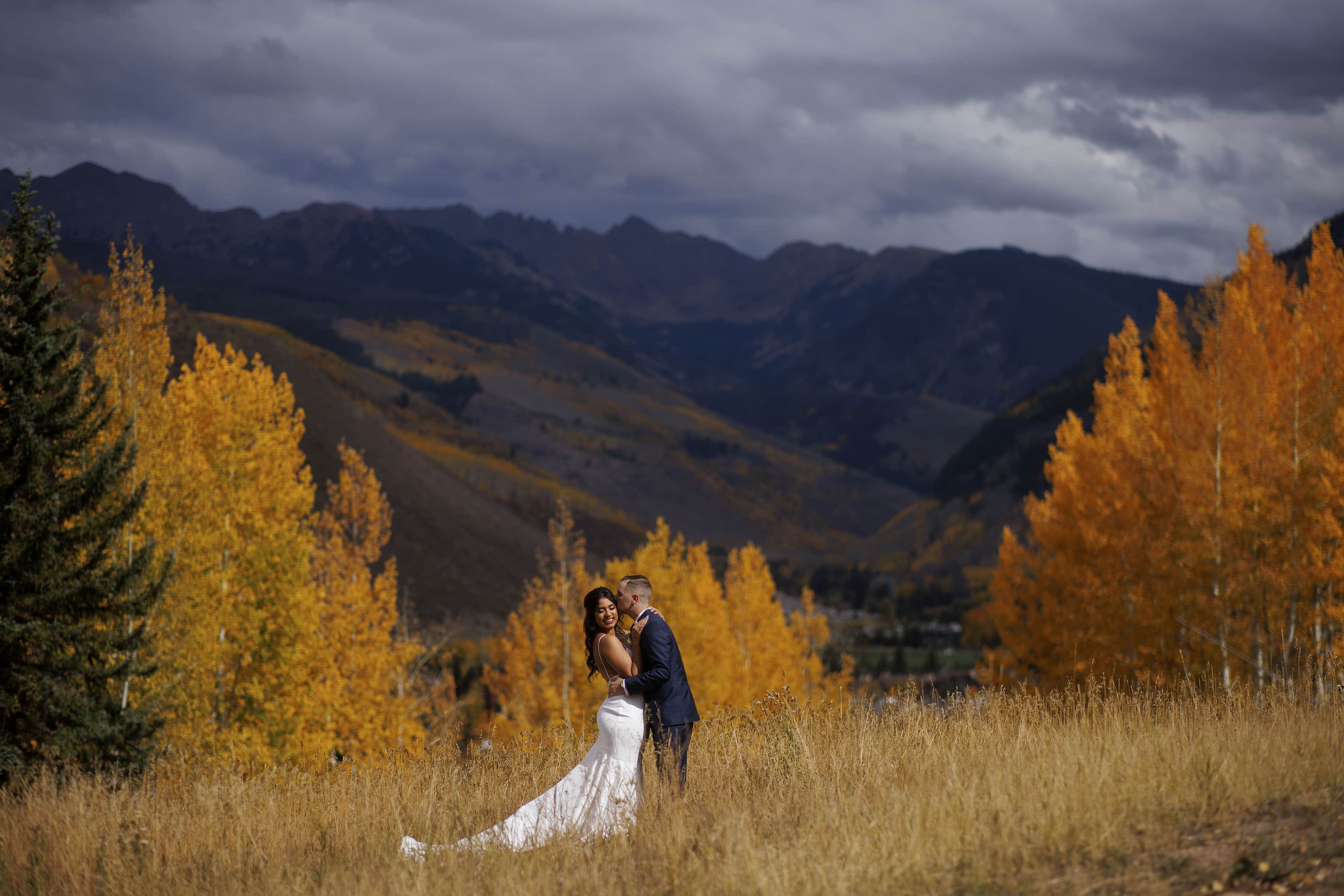 The bride and groom kiss in Vail surrounded by fall colors and the Gore Range on their wedding day