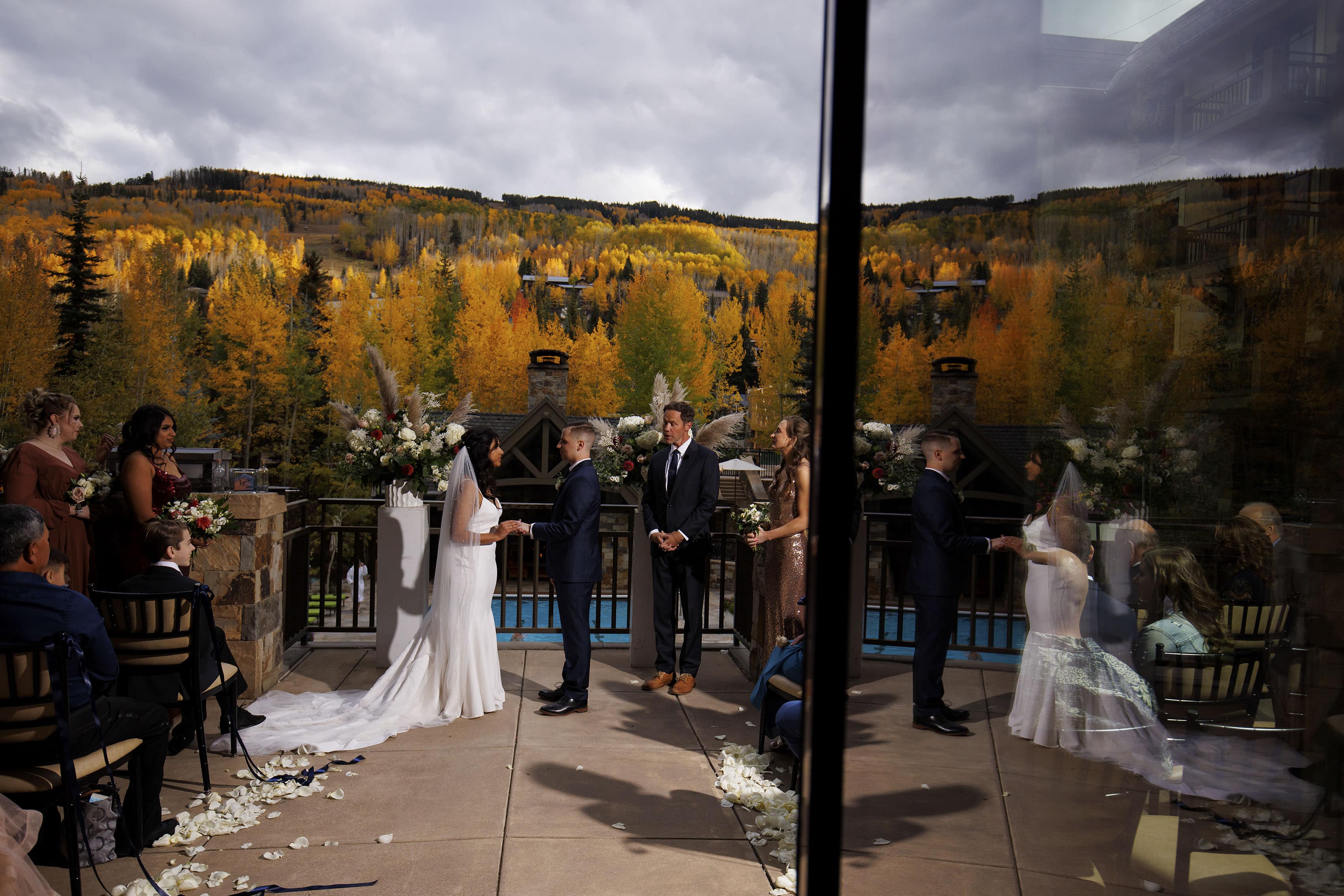 The bride and groom hold hands as the ceremony is reflected in a doorway at Four Seasons Resort and Residences Vail